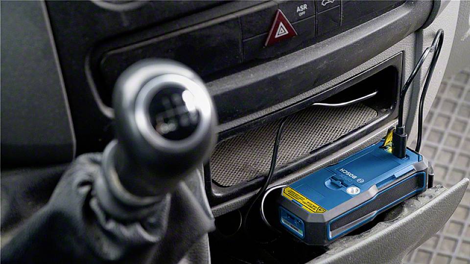 Modré elektronické zařízení s anténou umístěné v autě v přihrádce pod přístrojovou deskou vedle řadicí páky.
