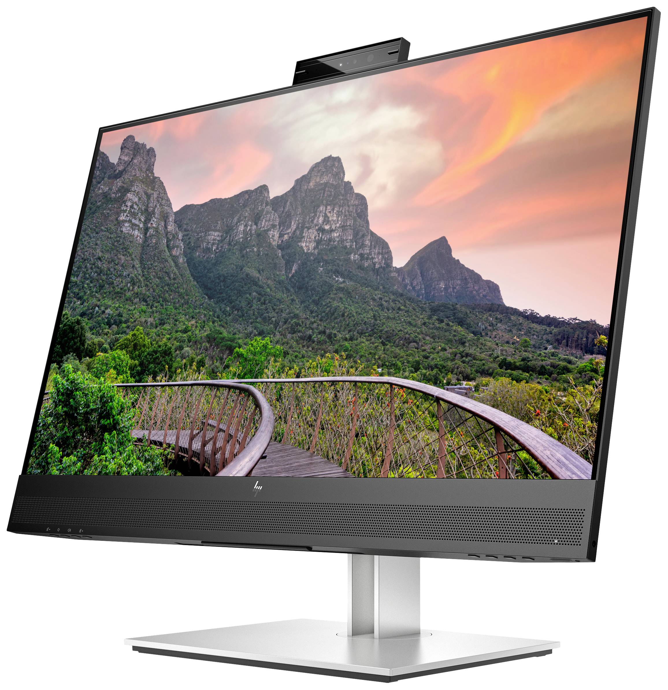 Monitor zobrazuje fotografii hor před barevným západem slunce. Dřevěný most vede skrz zelenou krajinou.