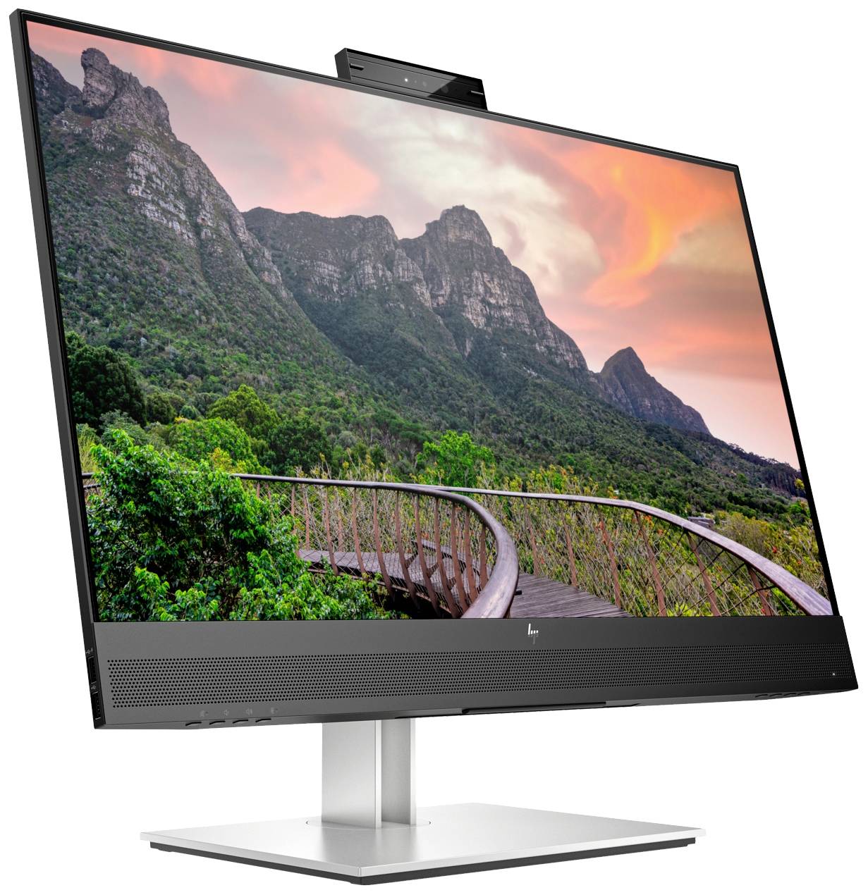 Monitor zobrazuje obraz horské panorama při západu slunce s dřevěným chodníkem vedoucím skrz bujnou zelenou vegetaci.