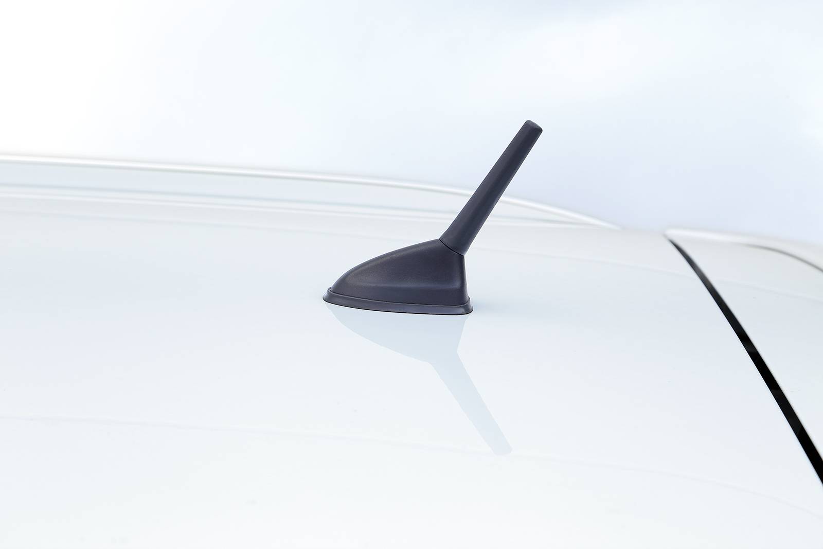 Autoanténa na bílé střeše automobilu před zatažnou oblohou.