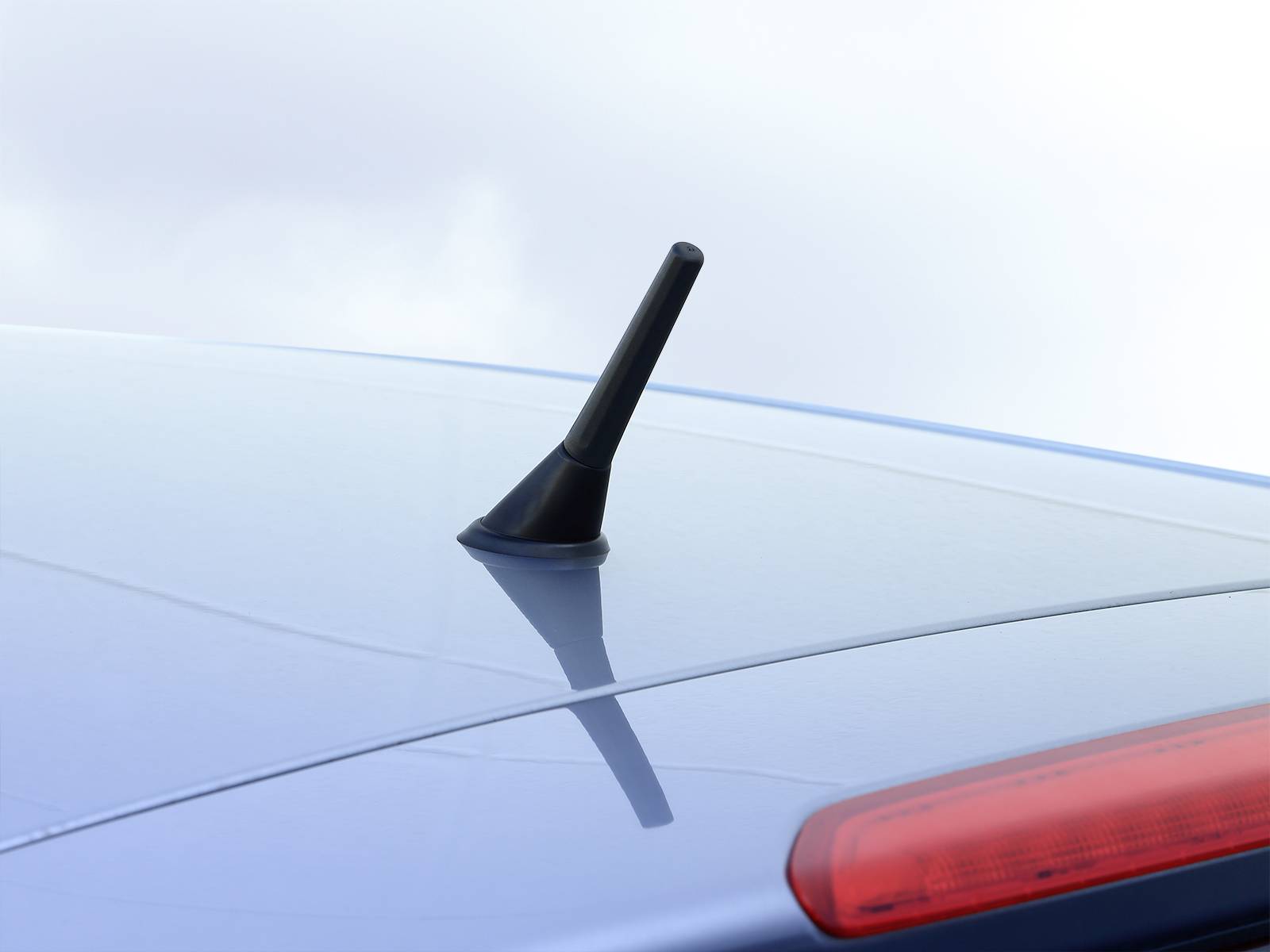 Krátká černá anténní tyč na střeše stříbrného automobilu, fotografovaná za zamračené oblohy.