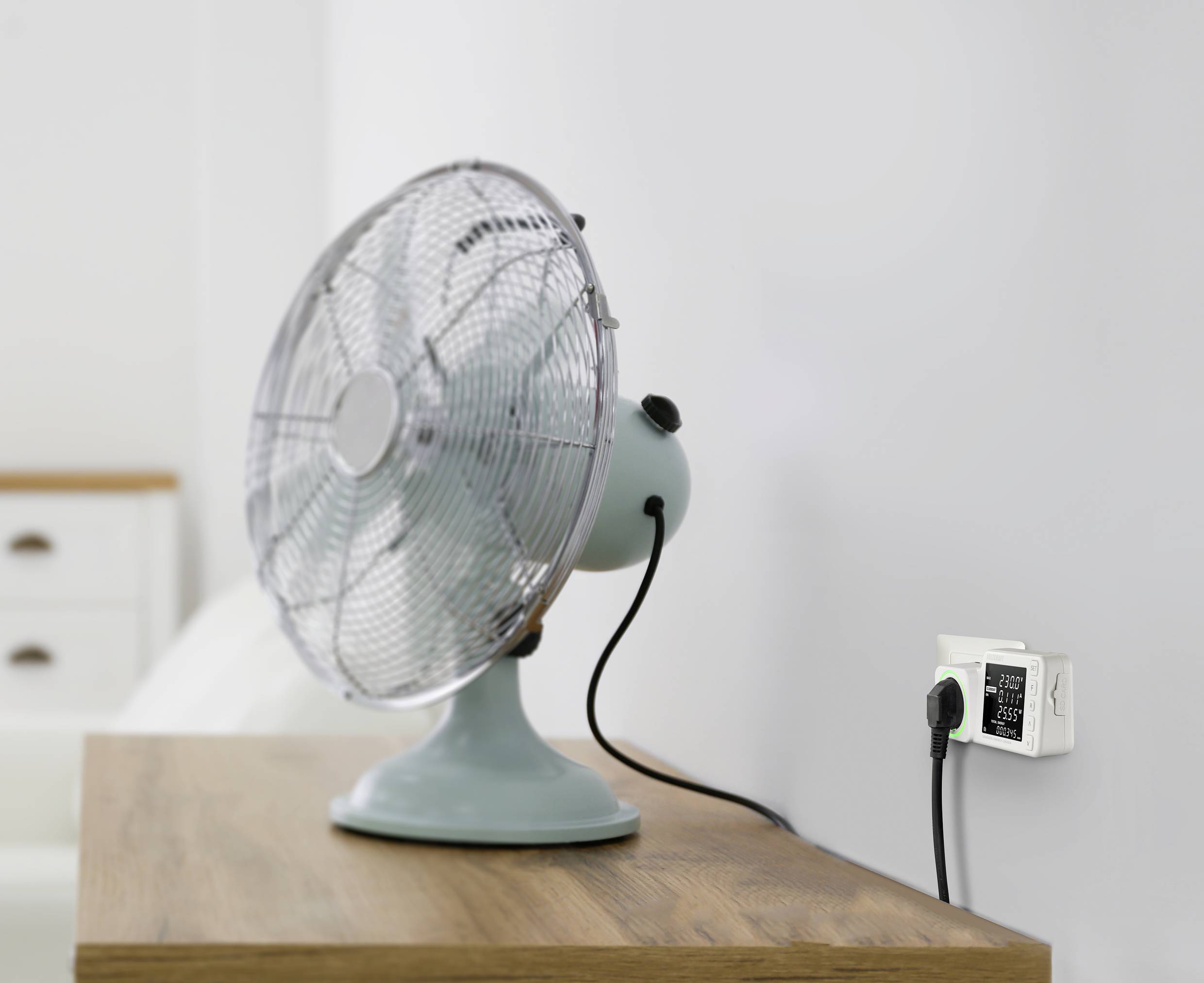 Stolní ventilátor na dřevěném stole je připojen k inteligentní zásuvce, která zobrazuje data o spotřebě energie.