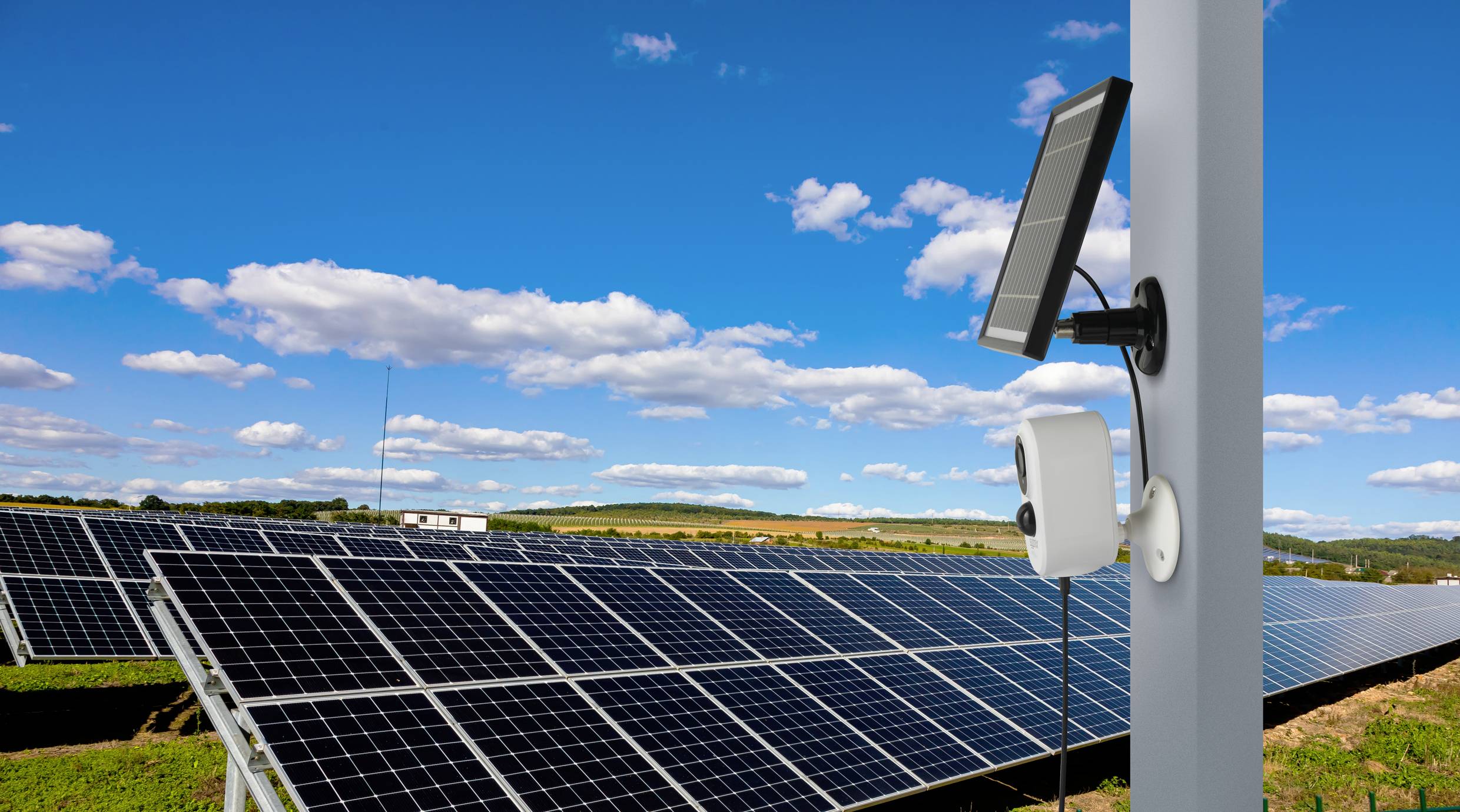 Solární elektrárna na poli pod modrou oblohou. V popředí kamera umístěná na sloupku.