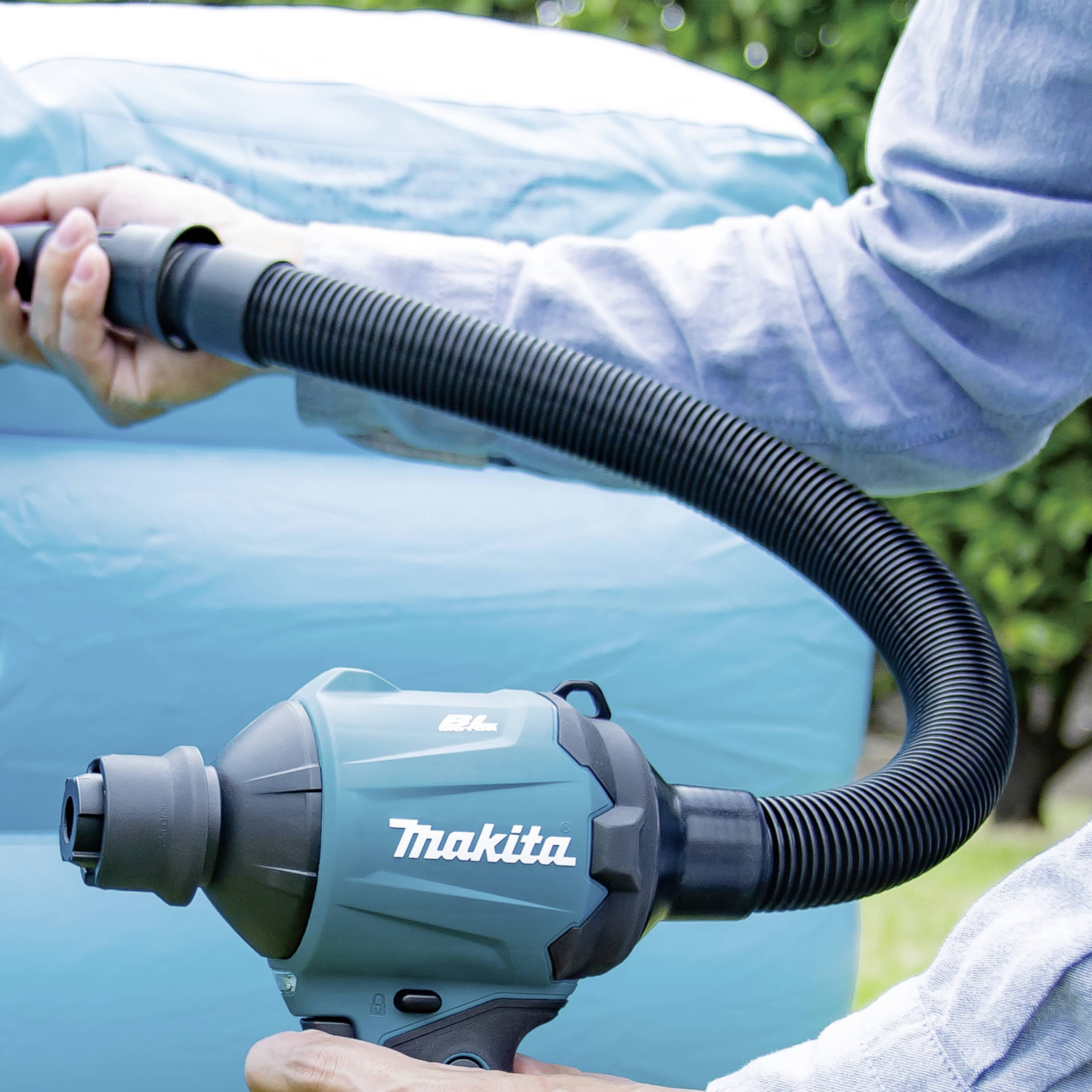 Jeden člověk drží elektrickou ruční pumpu a venku nafukuje velký modrý nafukovací předmět.