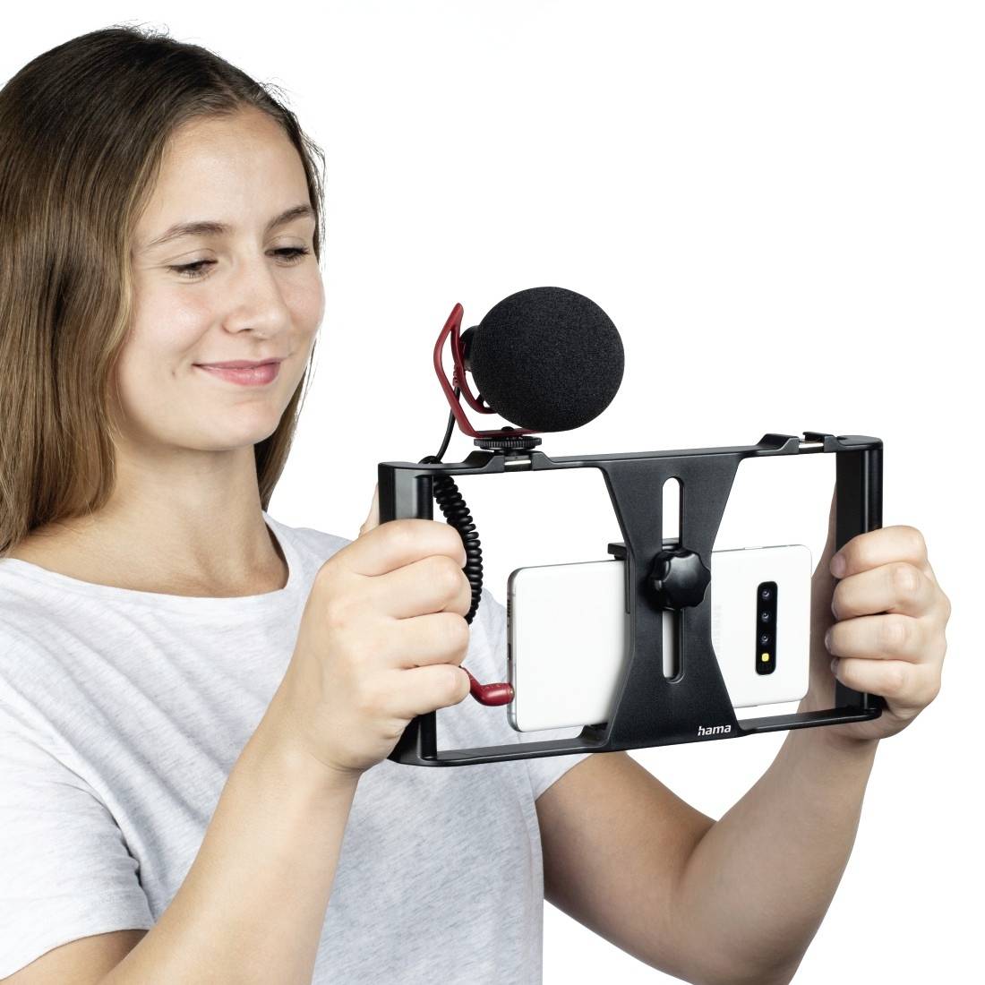 Žena drží smartphone ve stojánku s mikrofonem, připravená k nahrávání. Hlavní pozornost je věnována přípravě zařízení pro mobilní videonahrávky.