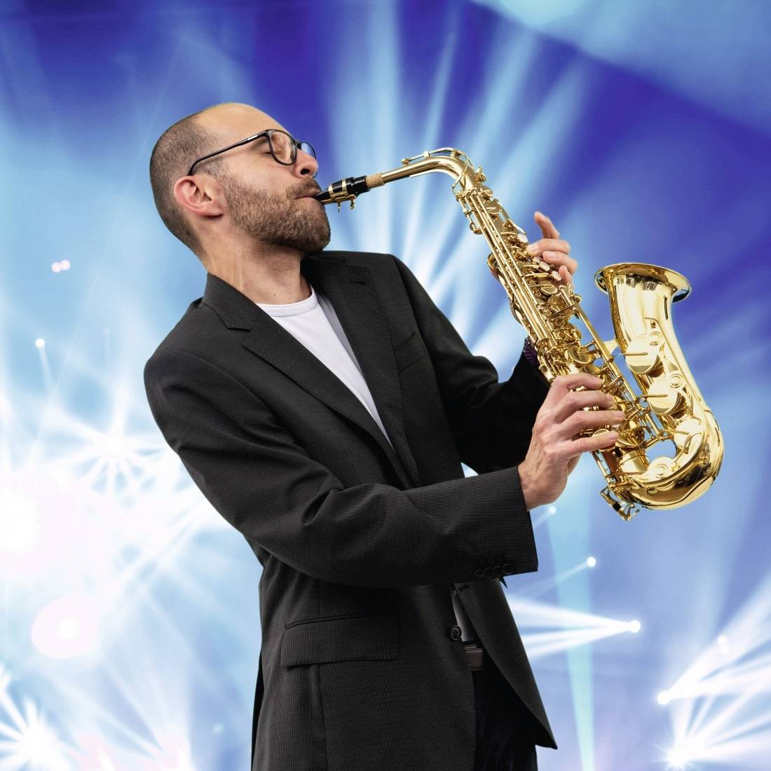 Muž v obleku hraje na saxofon na pódiu s barevnými světly v pozadí, což vytváří veselou a dynamickou atmosféru.