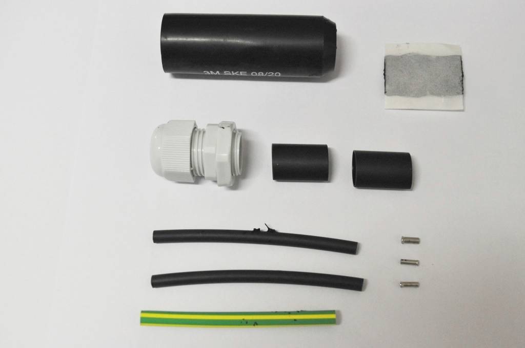 Elektrická instalační sada s kabely, zástrčkami, svorkami a izolačním materiálem uspořádaná na bílém pozadí.