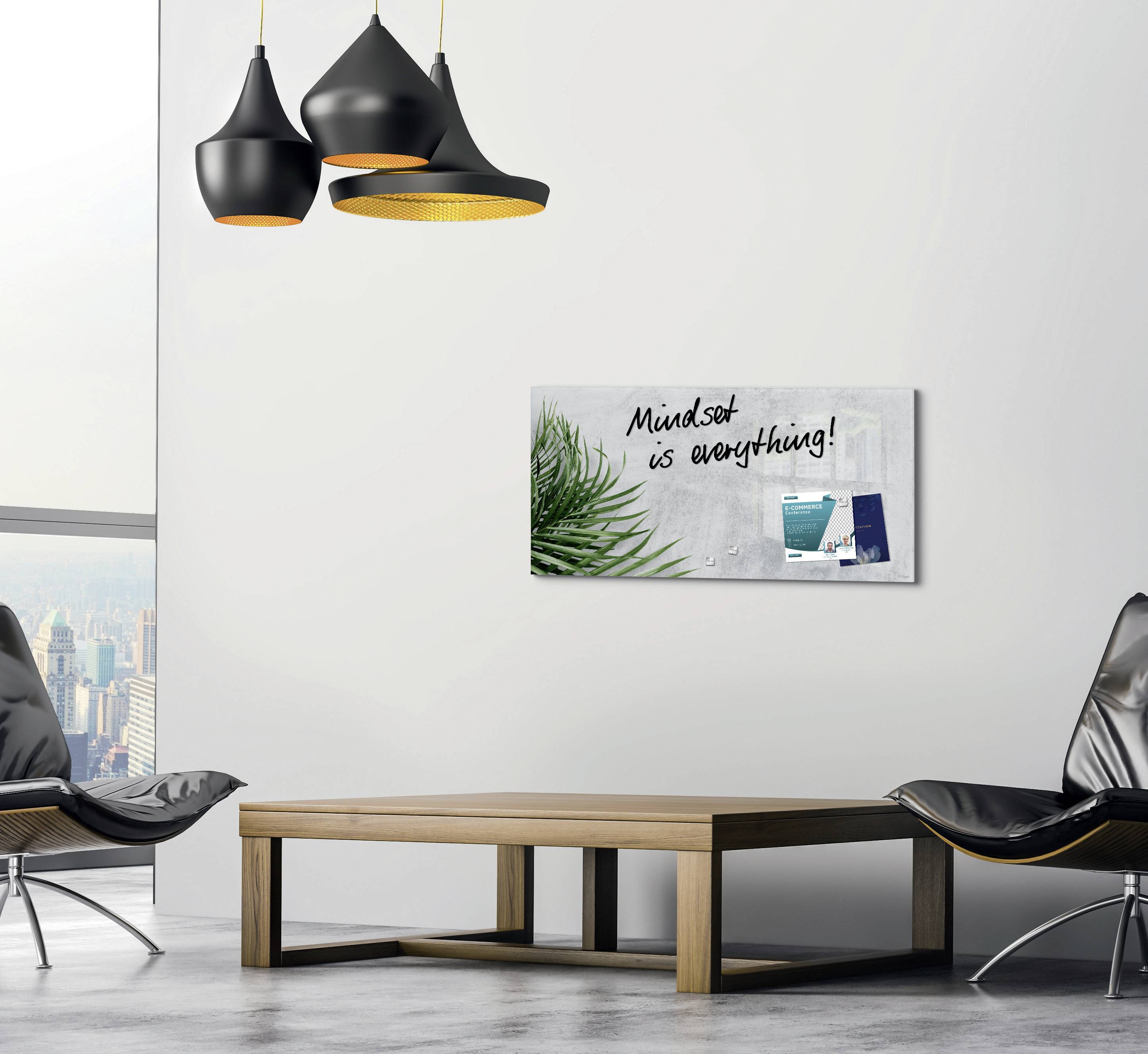 Obývací pokoj s moderními černými lampami, minimalistickým dřevěným stolem a šedou židlí. Na stěně visí obraz s nápisem 'Mindset je všechno!', list papíru a kancelářské potřeby.