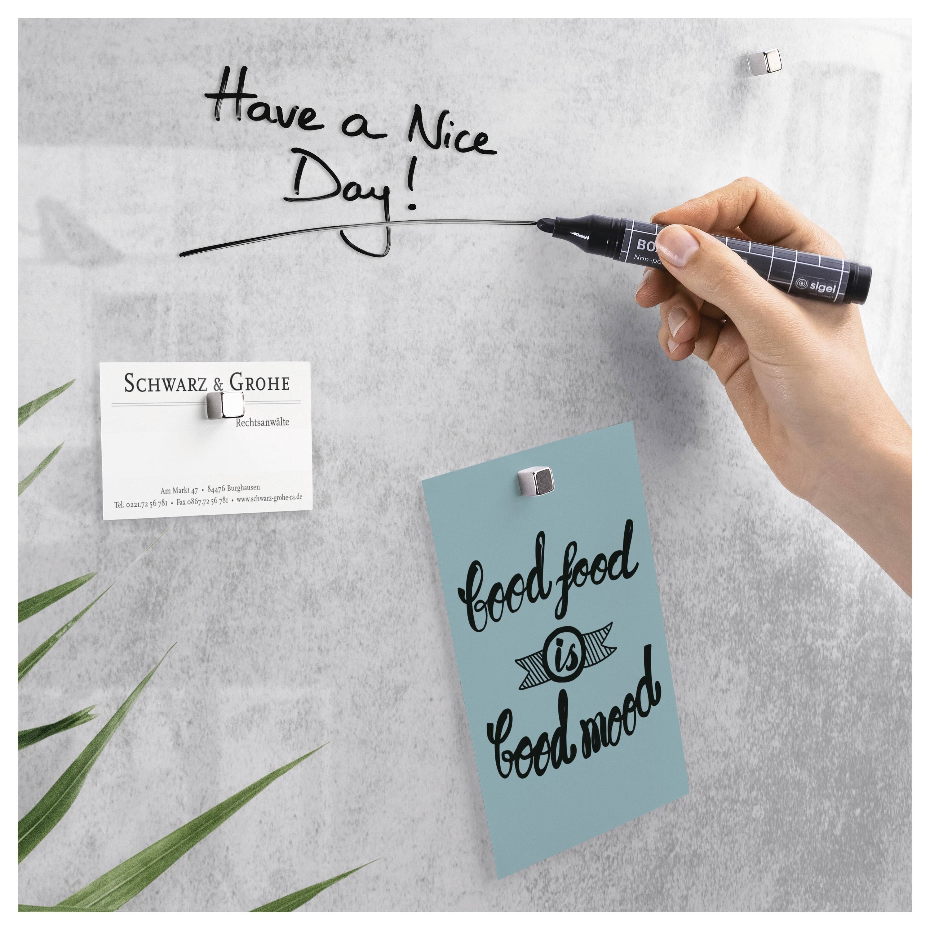 Ruka píše na bílou tabuli „Have a Nice Day!" vedle dvou magnetem připevněných kartiček, z nichž jedna nese nápis „Schwarz & Grohe" a druhá „food is good mood".