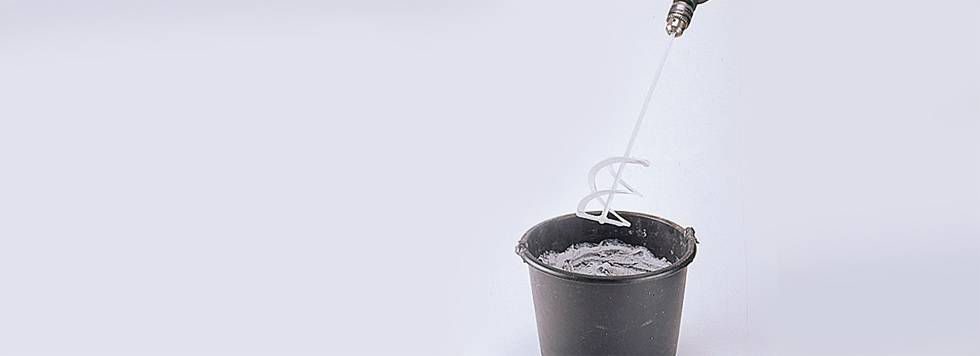 Míchač malty se otáčí nad černým kbelíkem s cementovou směsí, která je právě připravována.