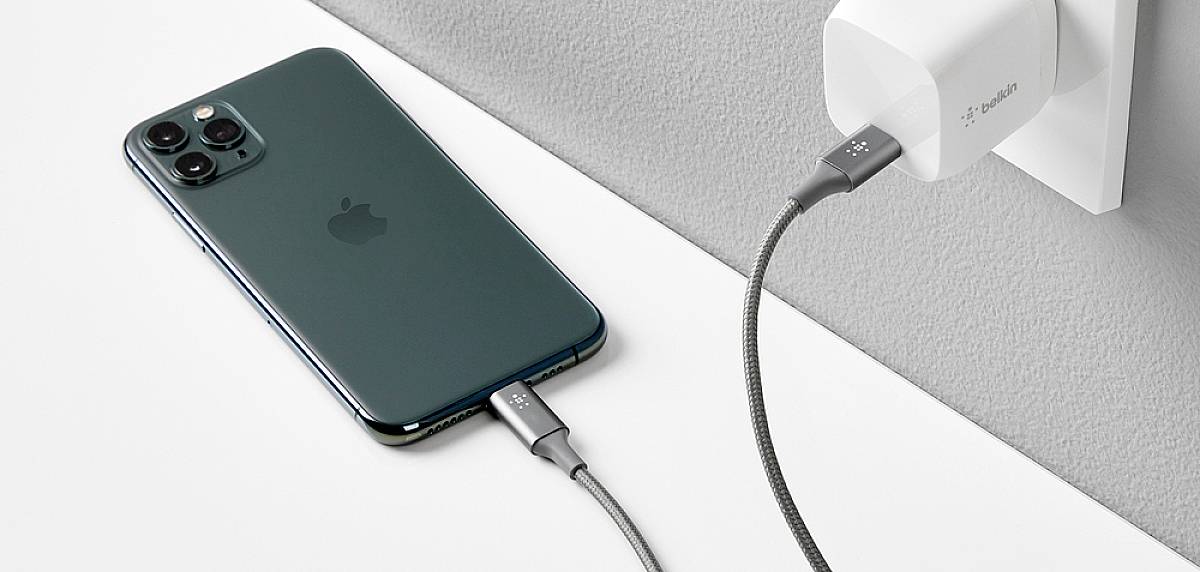 Smartphone je připojeno pletencem kabelu k nabíječce, která je zapojena do elektrické zásuvky.