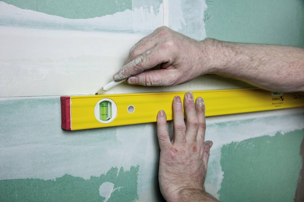 Jedna osoba kontroluje vyrovnání zelené stěny pomocí vodováhy a spárovací hmoty.