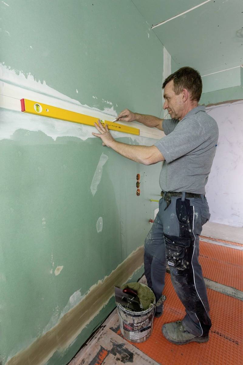 Muž kontroluje pomocí vodováhy rovnost stěny, zatímco pracuje v nedokončené místnosti.