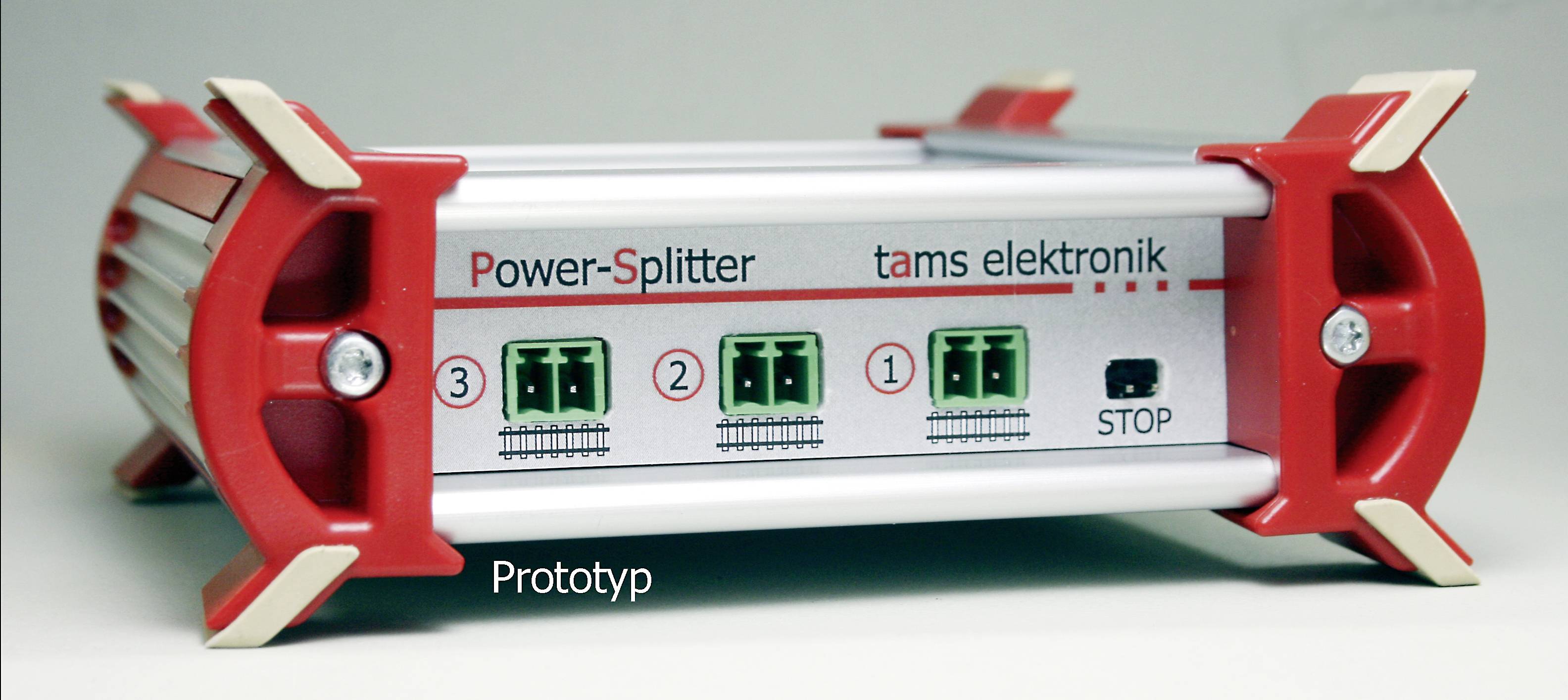 Červenobílé zařízení s nápisem 'Power-Splitter tams elektronik'. Má připojení a přepínač označený 'STOP'. Níže je napsáno 'Prototyp'.