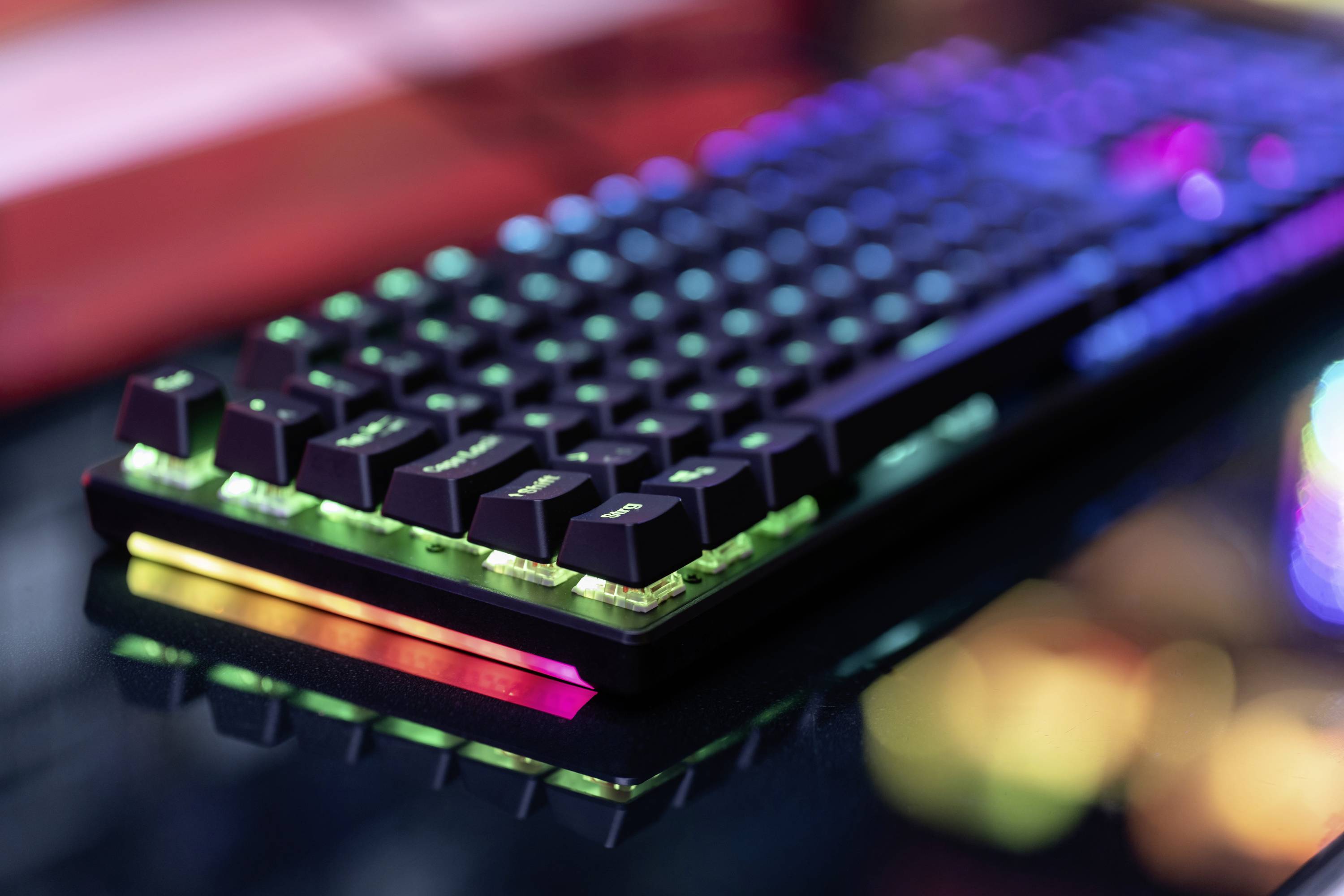 Herní klávesnice s barevnými RGB podsvícenými klávesami na tmavém stole. Barvy svítí živě a odrážejí herní atmosféru.