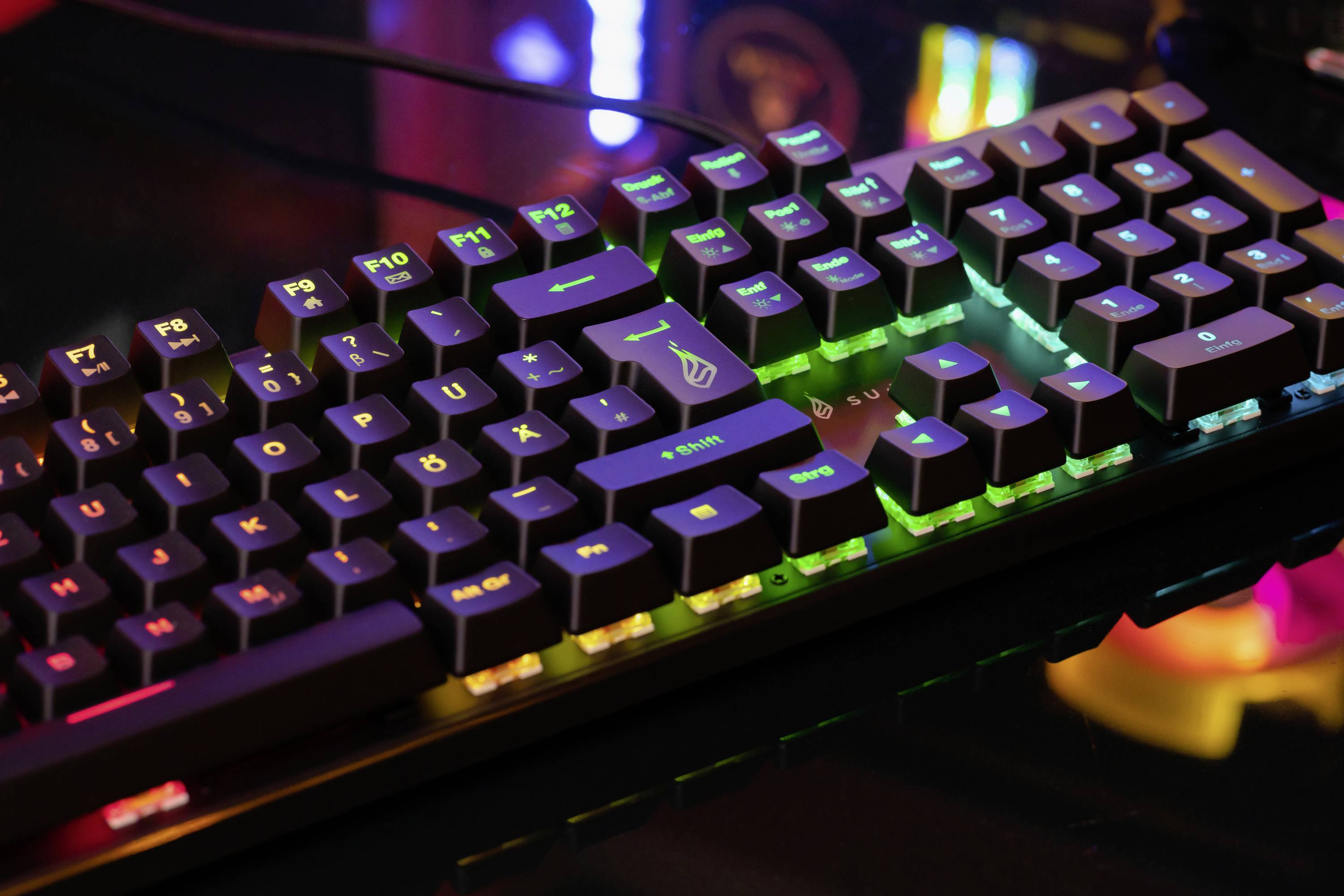 Mechanická klávesnice s barevným podsvícením RGB, která leží na stole.