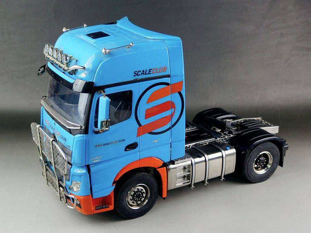 Modrý nákladní vůz s oranžovým zdobením a nápisem 'SCALE CLUB' na boku na šedém pozadí.