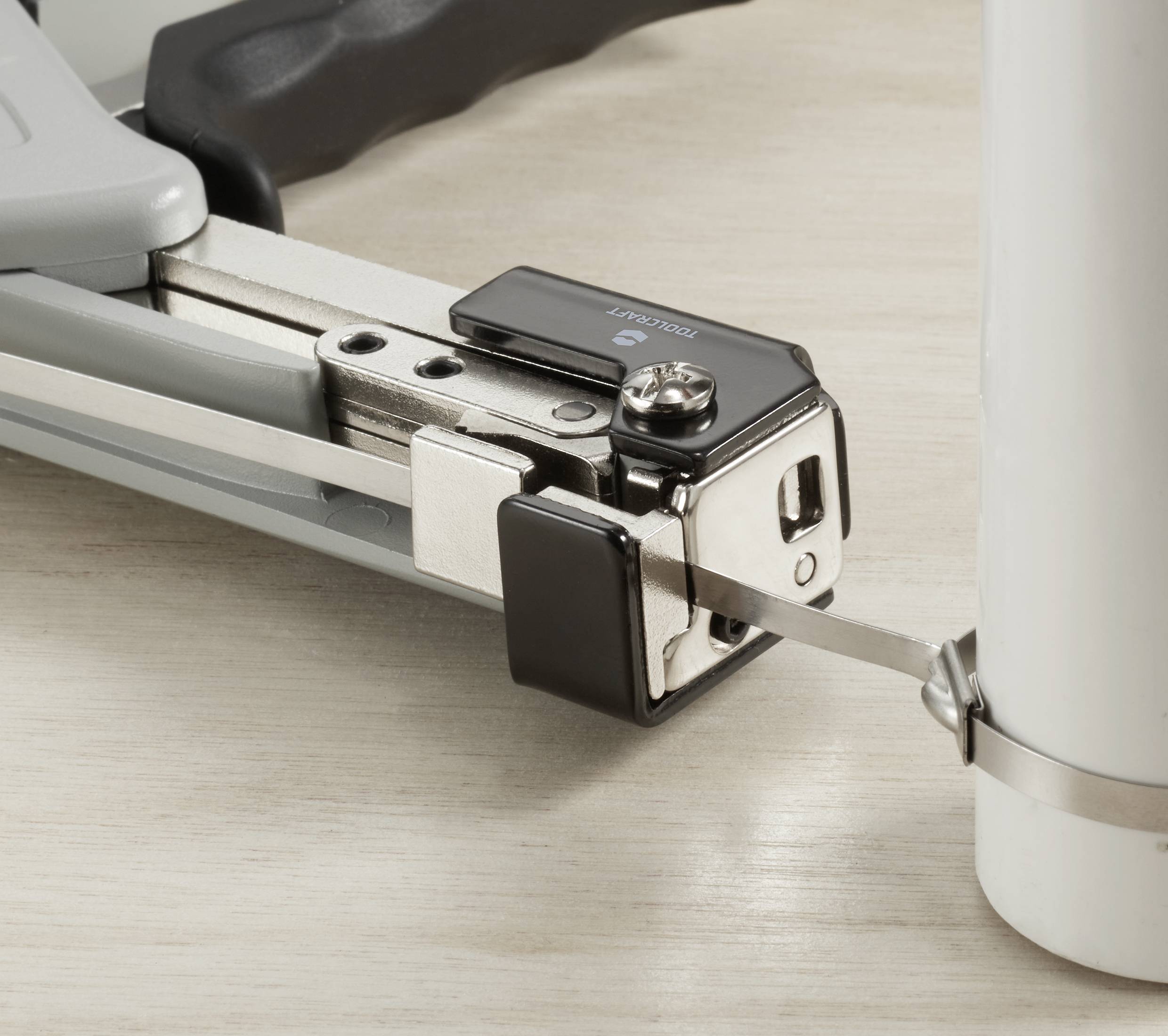 Napínací nástroj utáhne pásek kolem konce kulatého obalu, aby jej zajistil pro přepravu.