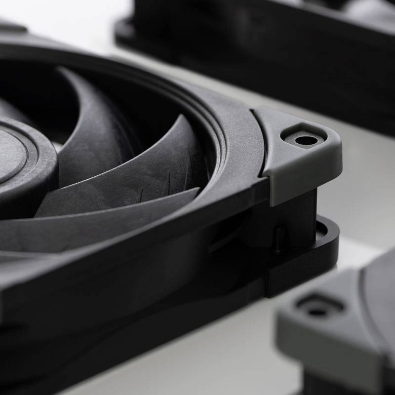 Černý počítačový ventilátor detailně zachycený zblízka, ležící na bílém podkladu. Snímek ukazuje detailně lopatky ventilátoru a jeho rám.