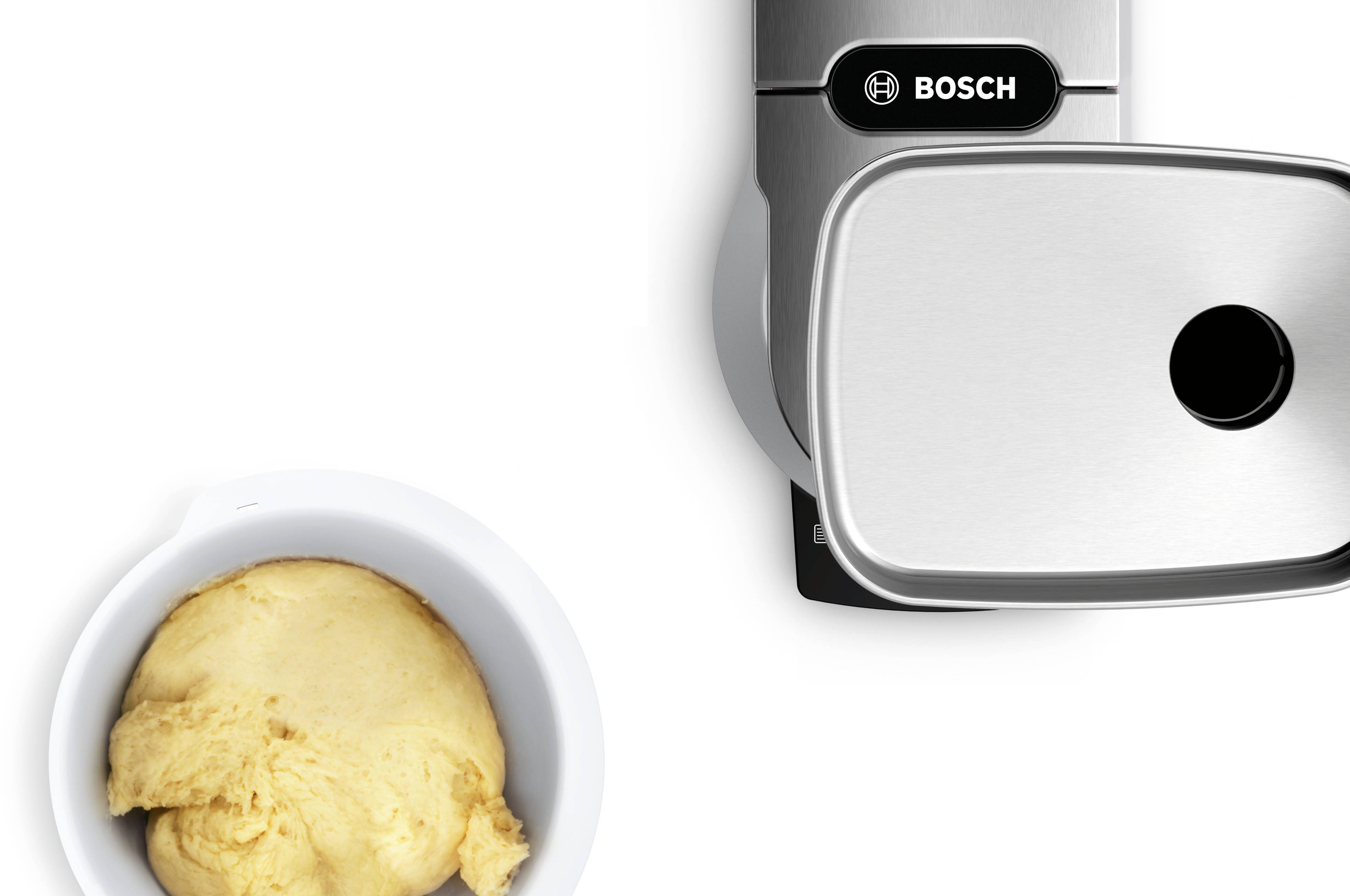 Těsto ve velké míse vedle moderního kuchyňského robotu.