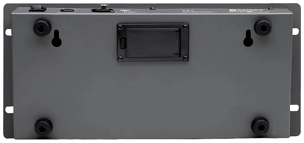 Šedé elektronické zařízení, zadní strana s prostorem pro baterie a montážními otvory. Nahoře jsou viditelné přípojky a spínače.
