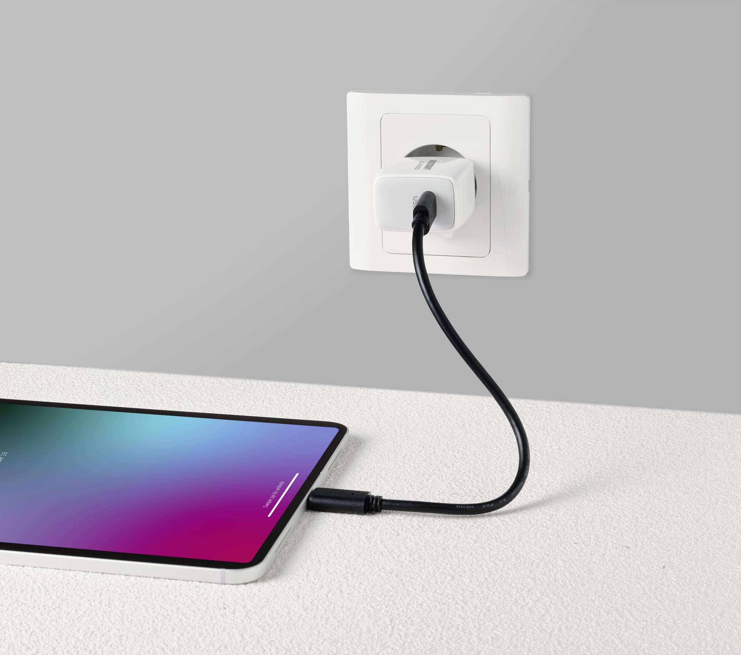 Na stole leží smartphone, který je připojen černým kabelem k nástěnné elektrické zásuvce a nabíjí se.