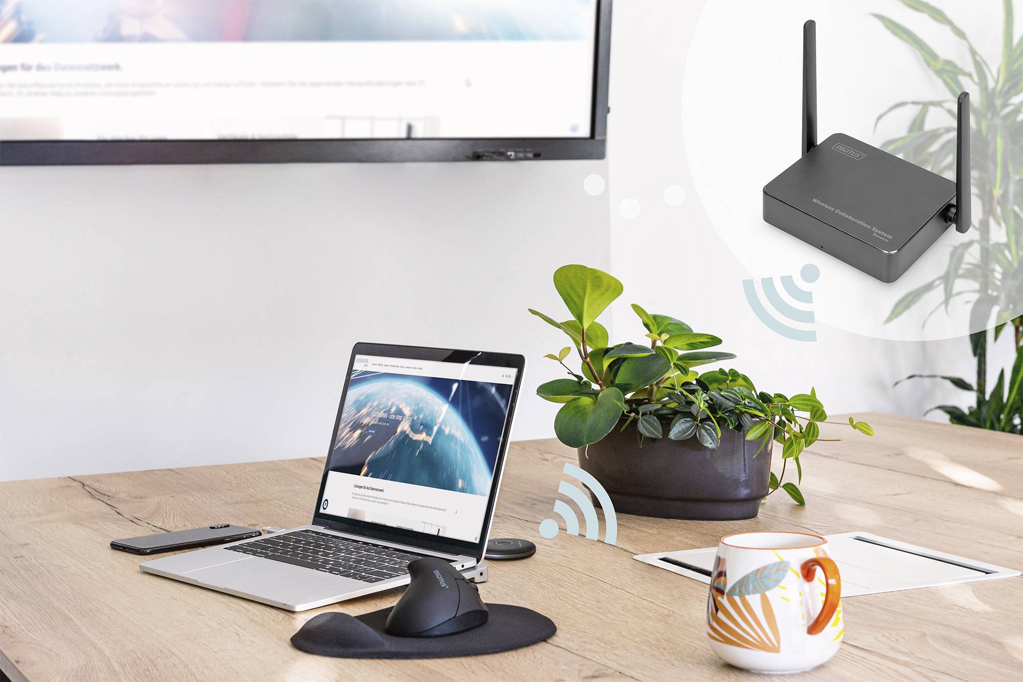 Laptop na stole zobrazuje mapové podání Země na obrazovce. WiFi router vysílá signál. V pozadí je monitor.