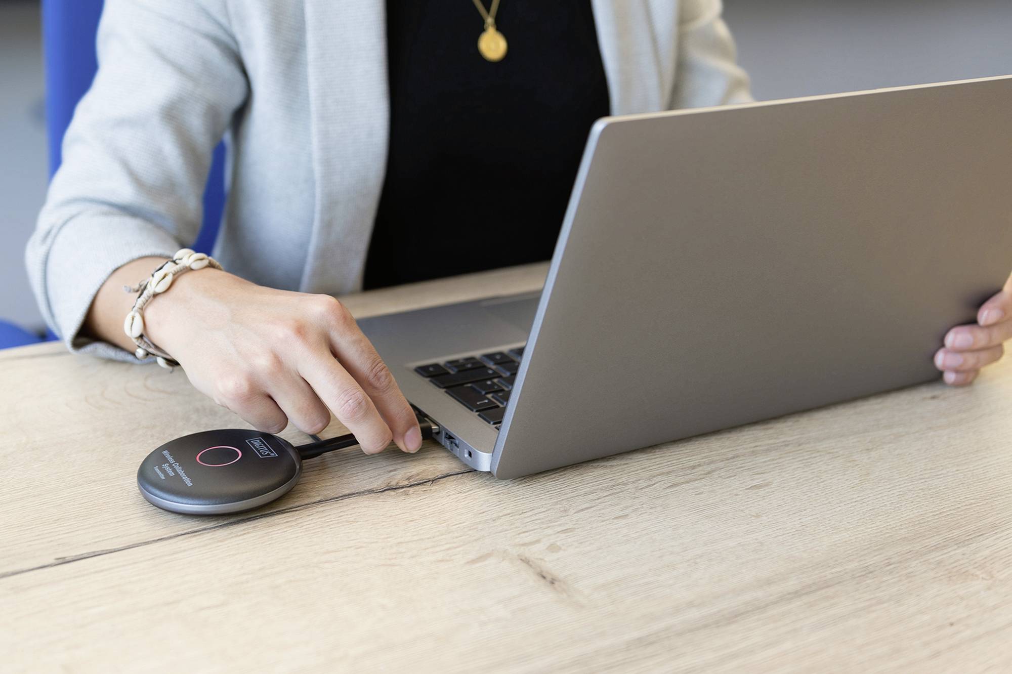 Osoba připojuje přenosné zařízení k laptopku pomocí kabelu na dřevěném stole.