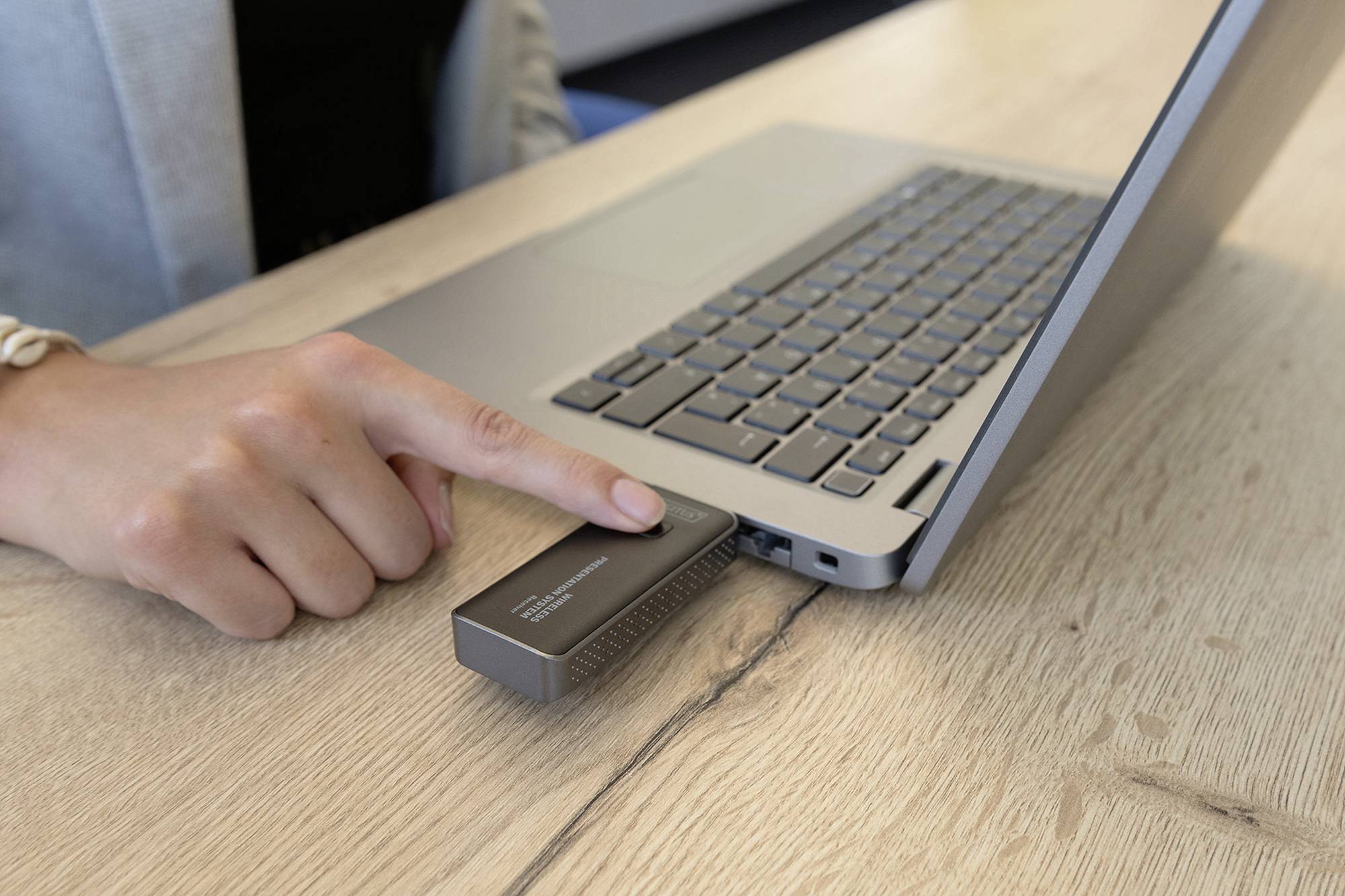 Osoba připojuje externí zařízení přes USB k laptopu za účelem přenosu dat. Zařízení leží na dřevěném stole.