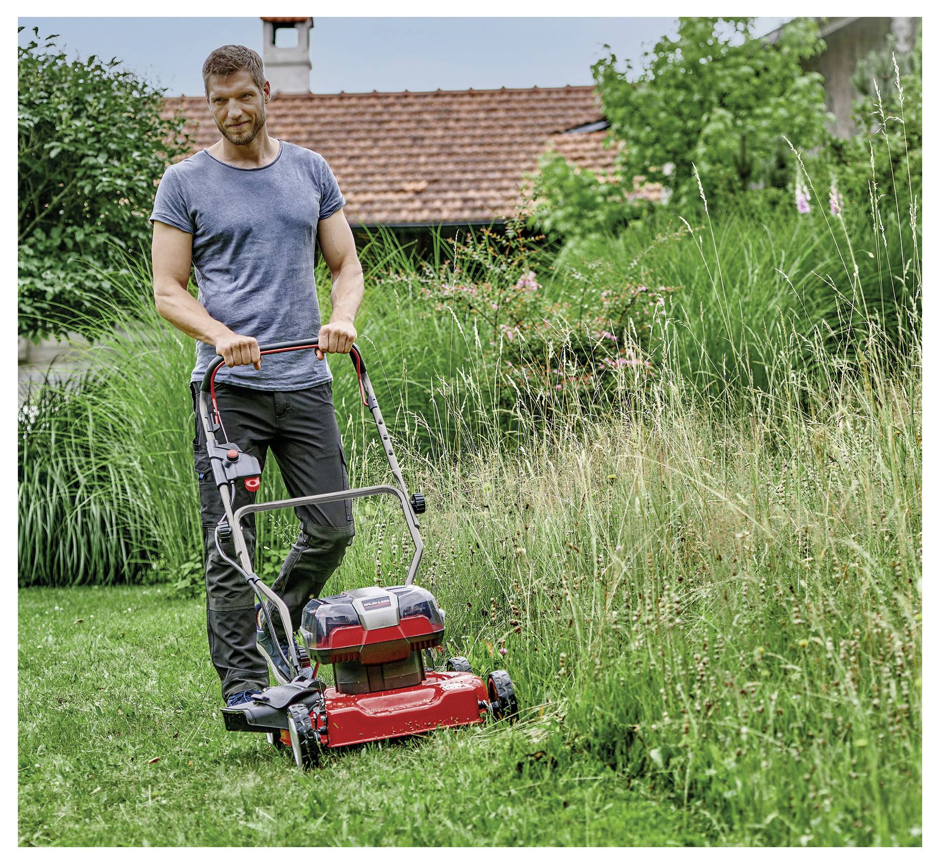 Červená sekačka na trávu z plastu a kovu s průhledným, odnímatelným krytem nahoře a stříbrnou rukojetí.