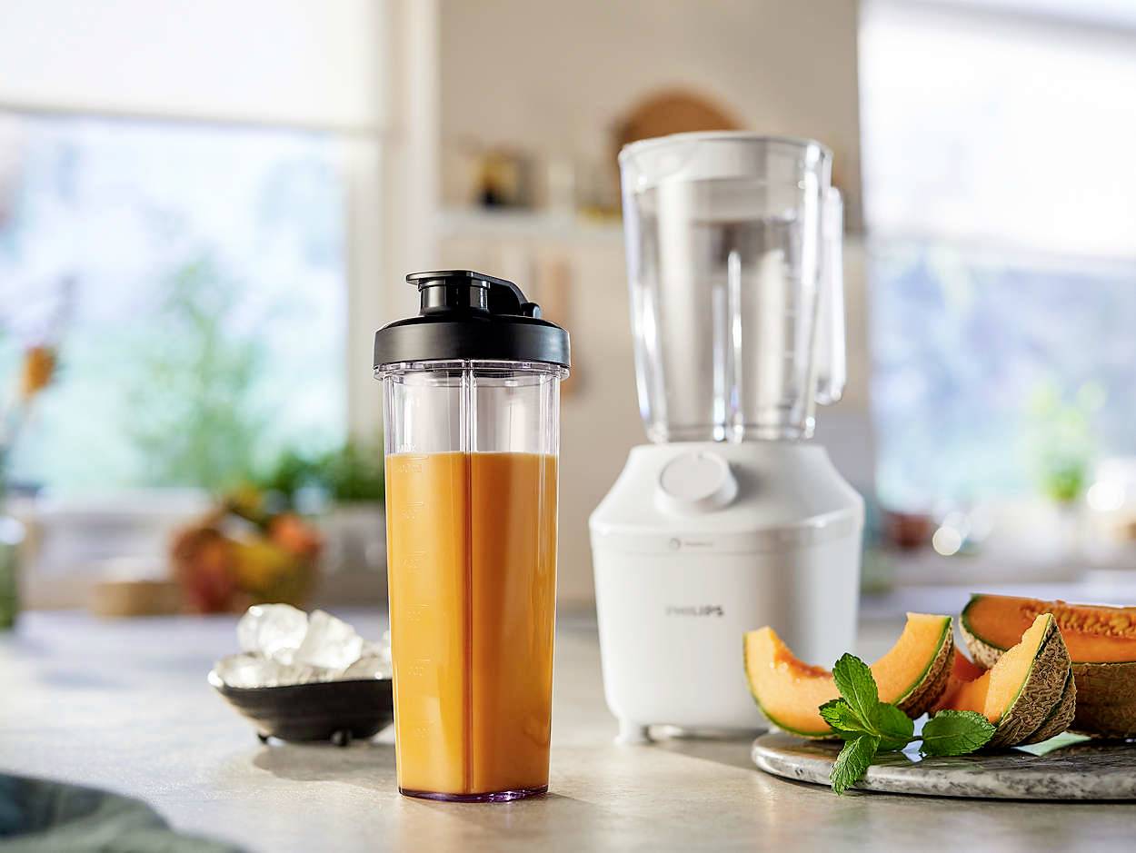 Mixér s pozadím z kostek ledu a sklenice čerstvého pomerančového smoothie v popředí, ozdobená plátky melounu.