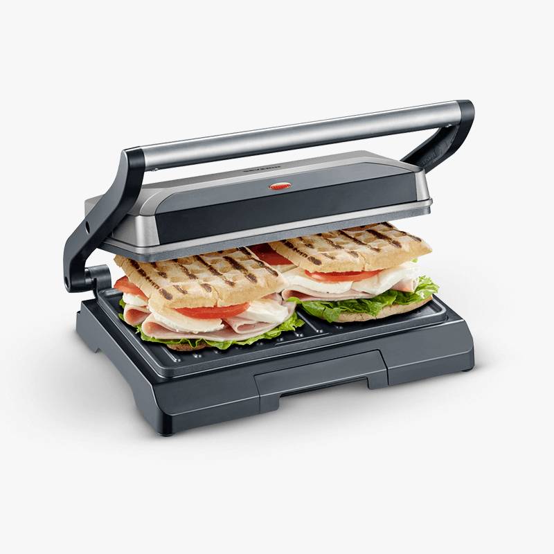 Elektrický panini gril se dvěma panini sendviči obsahujícími šunku, rajčata, salát a rozpuštěný sýr.