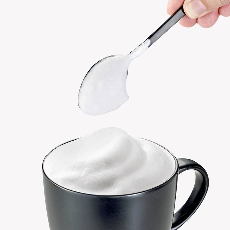 Lžíce s mléčnou pěnou je držena nad šálkem s napěněným mlékem.