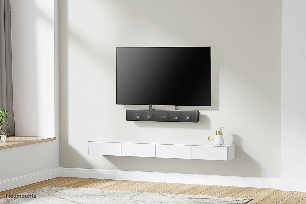 Plochý LED televizor a soundbar jsou zavěšeny na světlé stěně. Pod nimi je zavěšená komoda s dekorativními předměty.