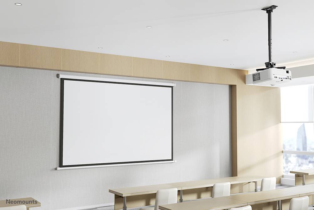 Konferenční místnost s projektorem zavěšeným na stropě, prázdné plátno vpředu a stoly se židlemi. Světlé, moderní zařízení.