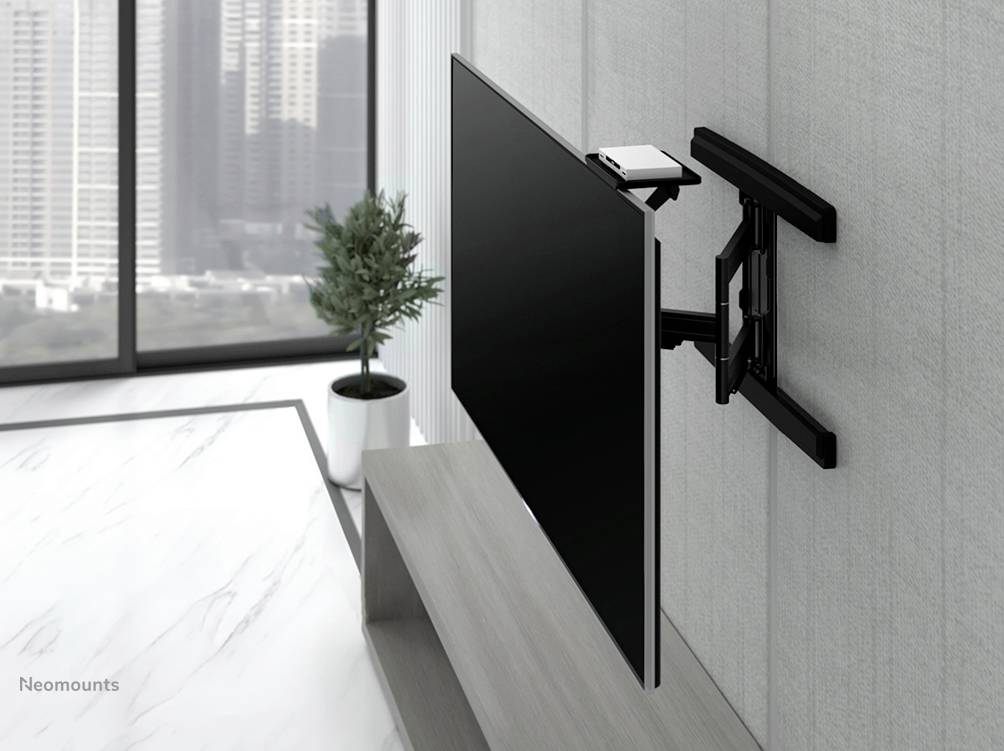 Plochý televizor je připevněn na otočném nástěnném držáku v moderním obývacím pokoji. V pozadí jsou viditelná okna s výhledem na město.