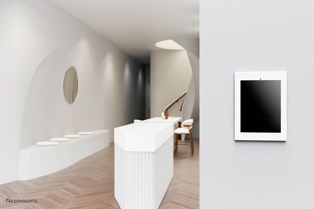 Světlý prostor s bílým recepčním pultem, tablet umístěný na stěně. Dřevěná podlaha, moderní design, minimalistické vybavení.