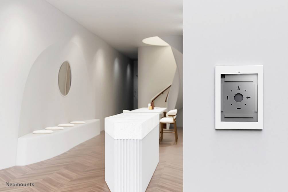 Moderní, minimalistický interiér s bílými stěnami a malým recepcním pultem. Na stěně visí obdélníkový šedý rám.