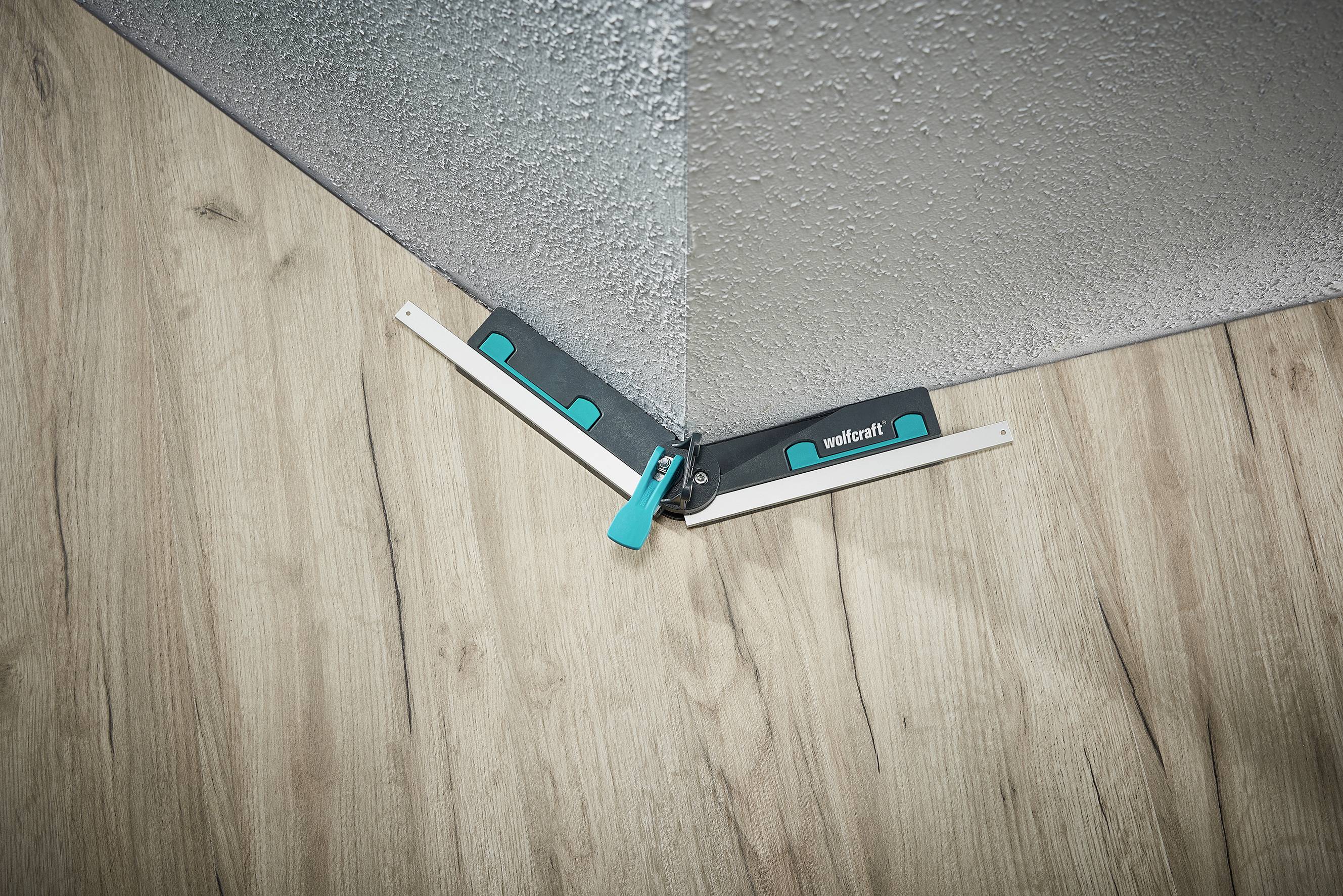 Úhloměr v rohu místnosti na dřevěné podlaze u šedé stěny, který přesně ukazuje úhel rohu.