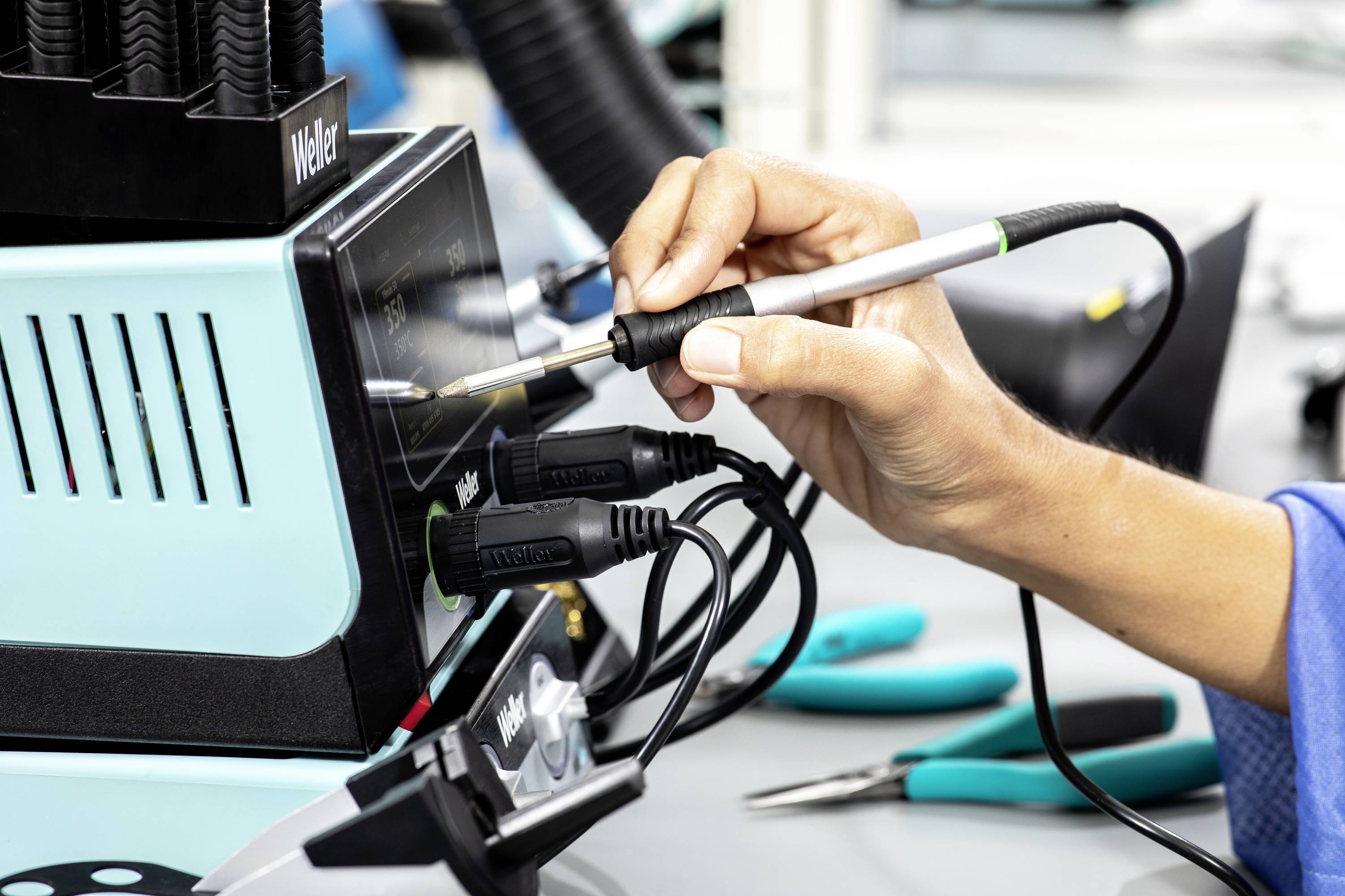 Osoba používá pájecí pero na elektrické pájecí stanici na pracovním stole s nástroji.