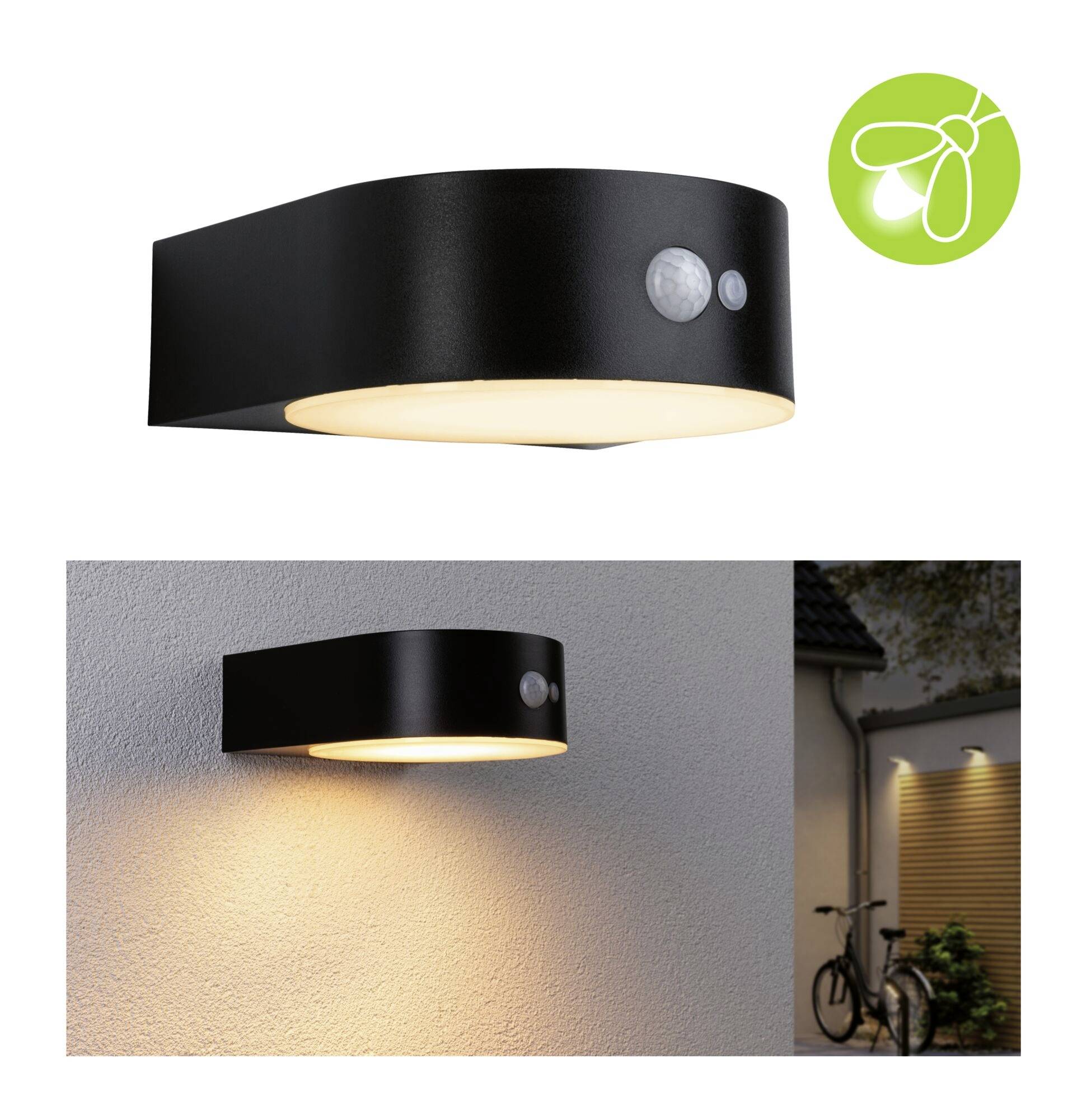 Černá, moderní venkovní lampa s pohybovým senzorem visí na zdi. Vyzařuje teplé světlo směrem dolů. V pozadí je vidět osvětlený dům.