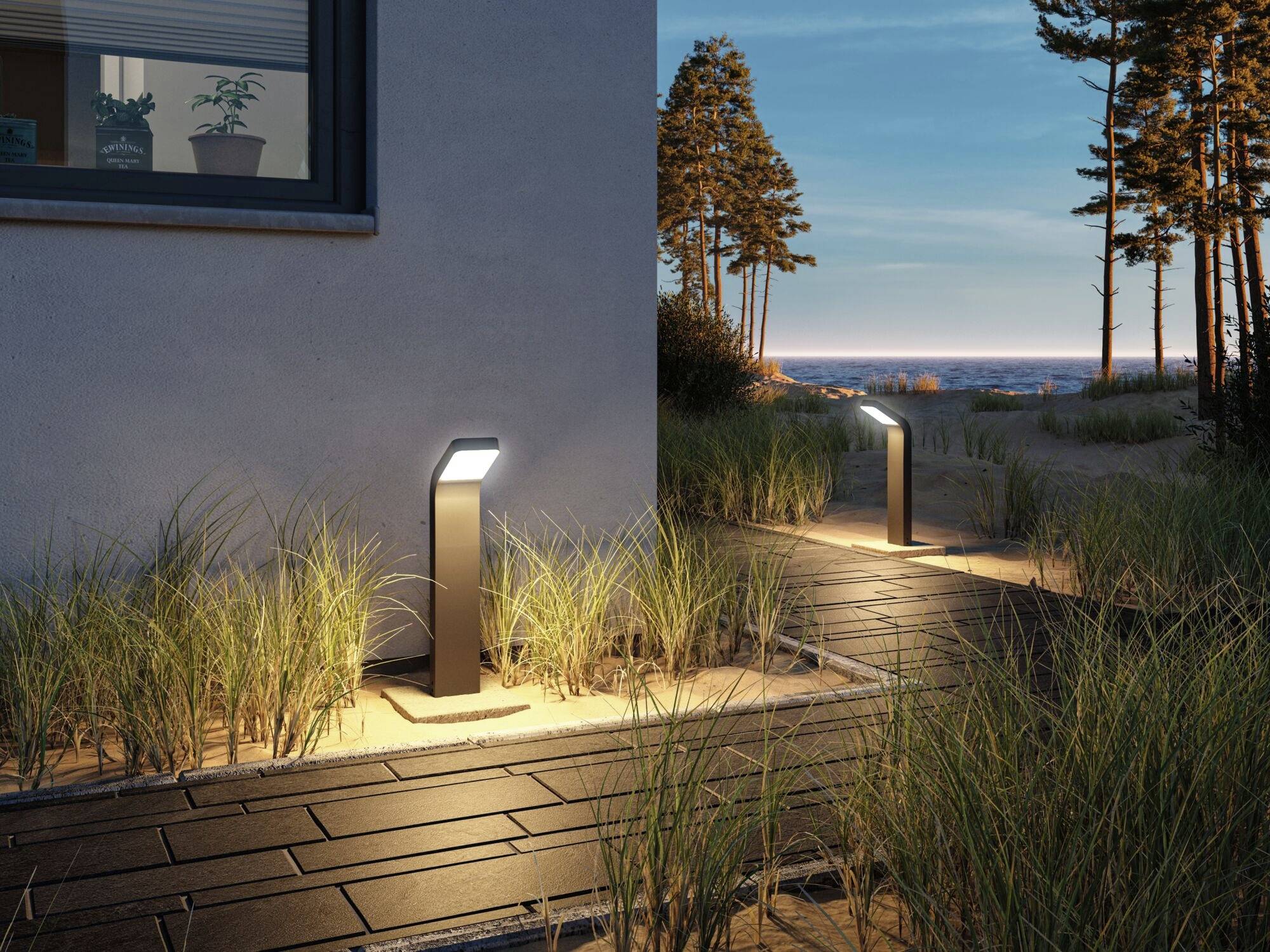 Cesta s moderními venkovními osvětleními a rostlinami vede kolem budovy směrem k moři za soumraku.