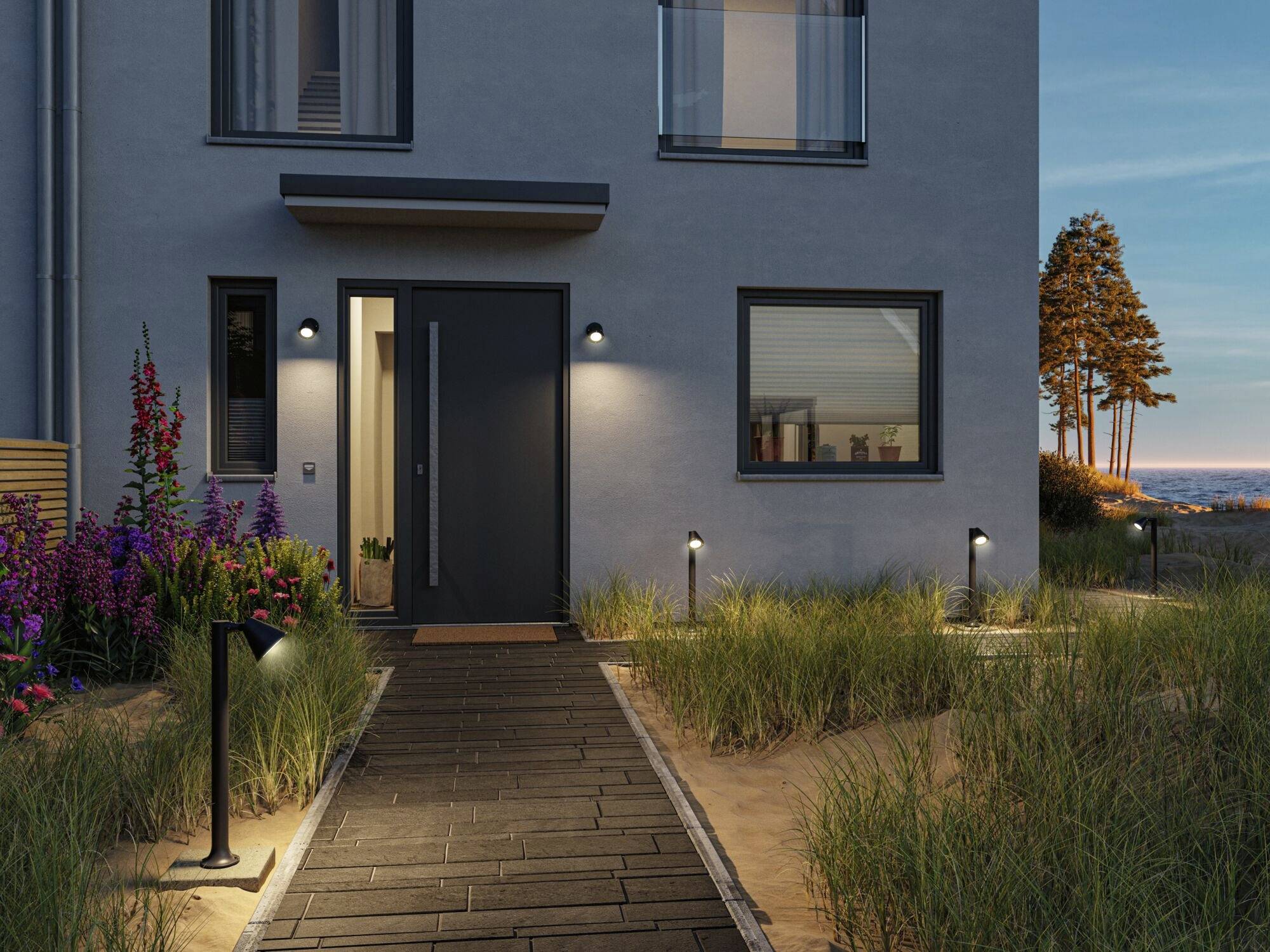 Vstupní prostor moderního domu za soumraku, s osvětlenou dřevěnou cestou, obklopený trávami a květinami.