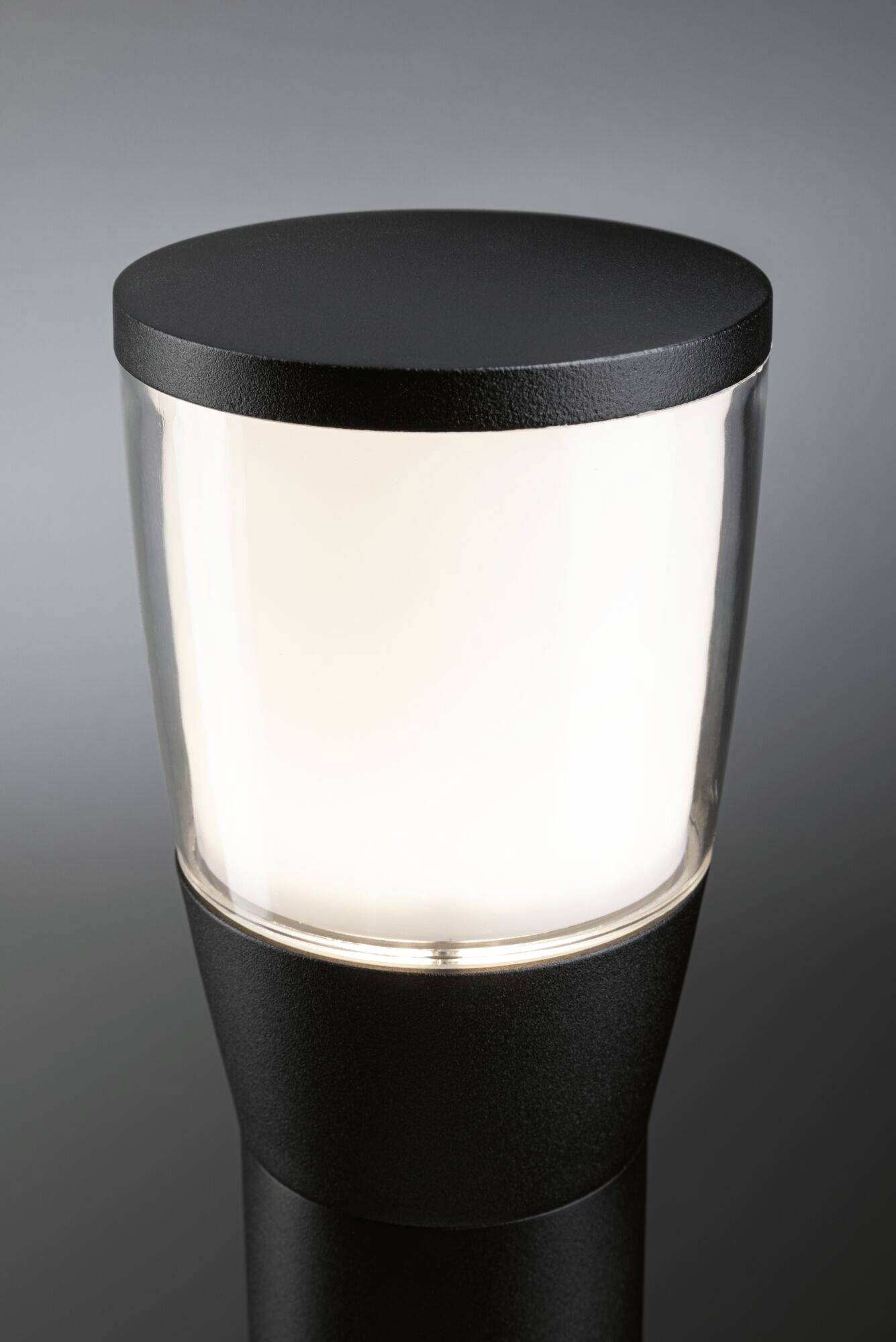 Venkovní svítidlo s moderním designem, černým tělem a průhledným stínidlem, osvětlující neutrálně bílým světlem.