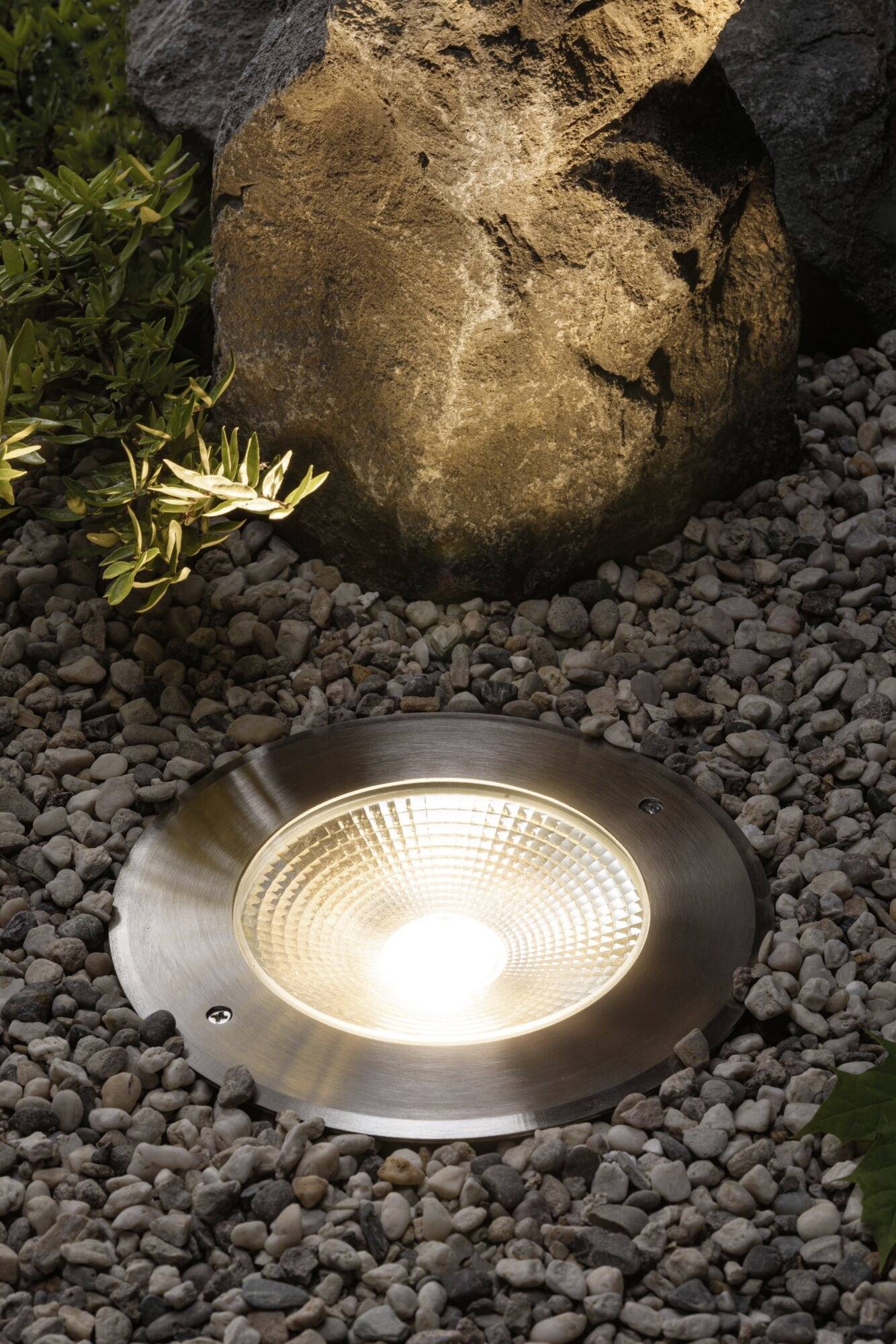 Zapuštěné zahradní osvětlení dekorativně osvětluje kámen a okolní oblázky v zahradě.