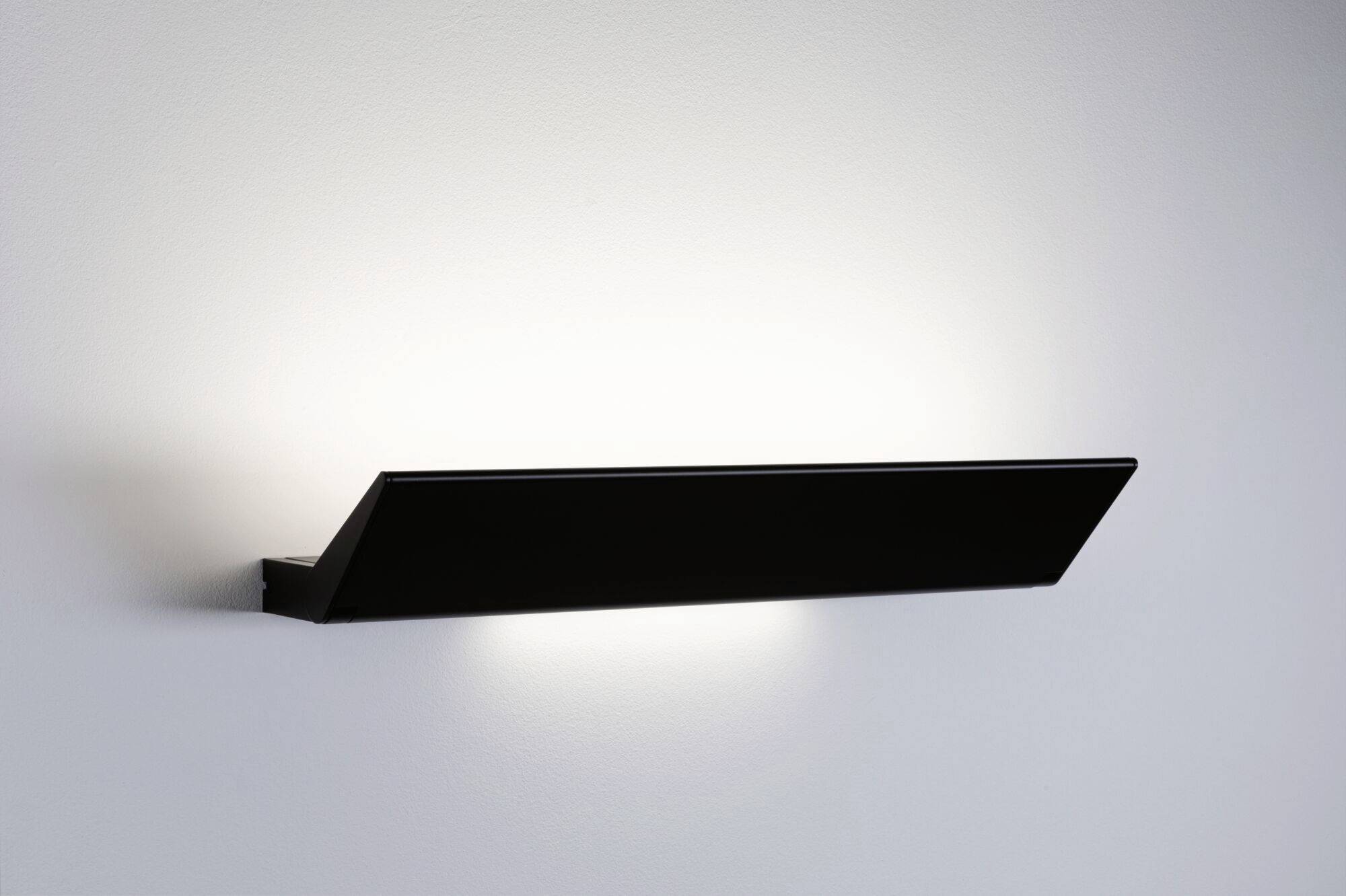 Jednoduchá, moderní nástěnná lampa svítí nahoru a měkce osvětluje stěnu.