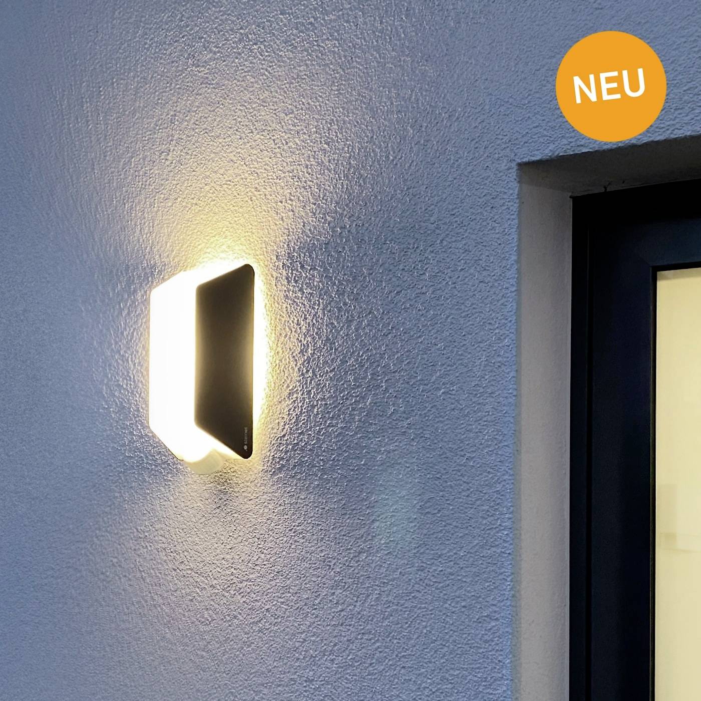 Moderní venkovní osvětlení na zdi vedle okna. Nahoře vpravo symbol 'NOVINKA'.