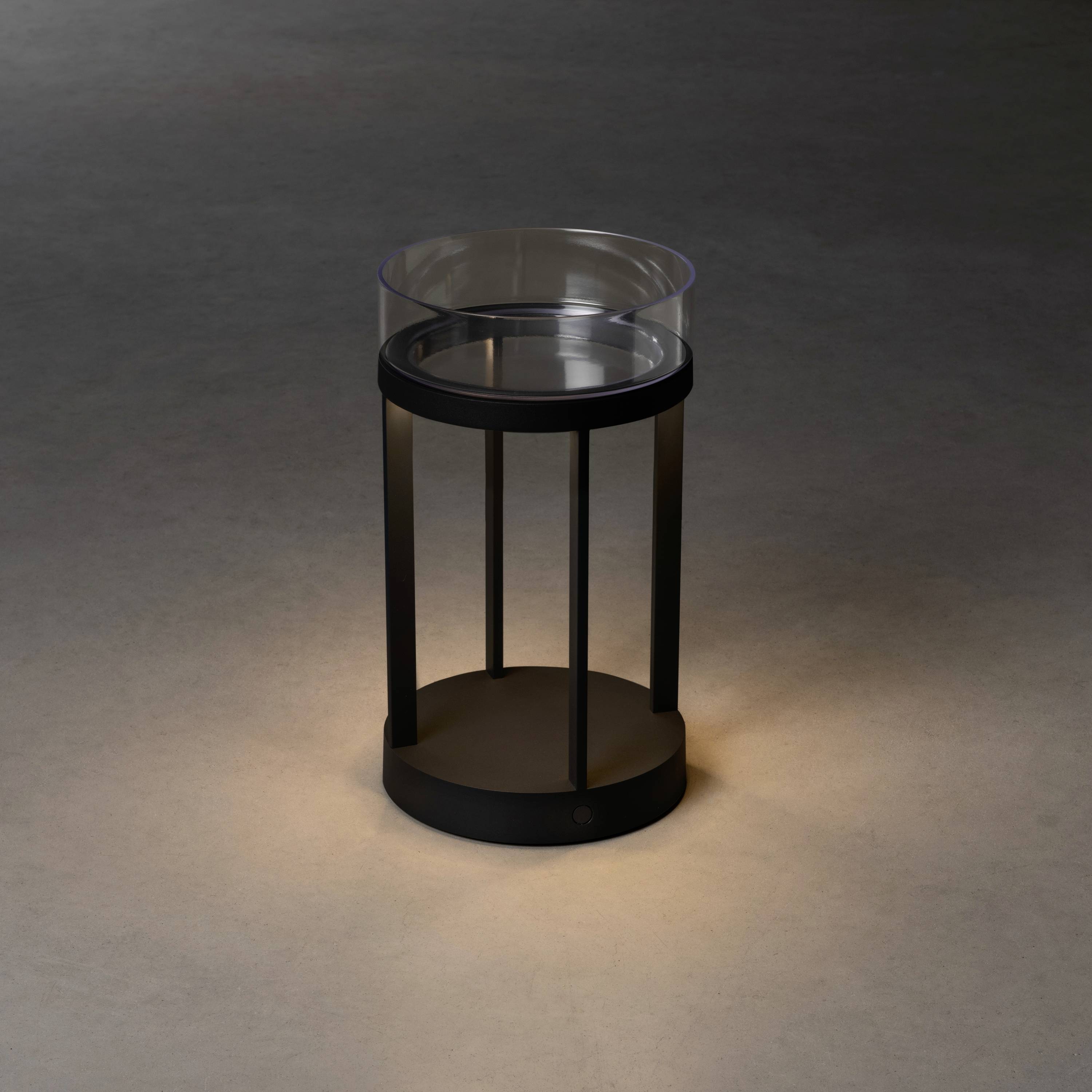 Malý, kulatý, černý odkládací stolek se skleněnou deskou stojí na tmavé dřevěné podlaze. Minimalistický design.