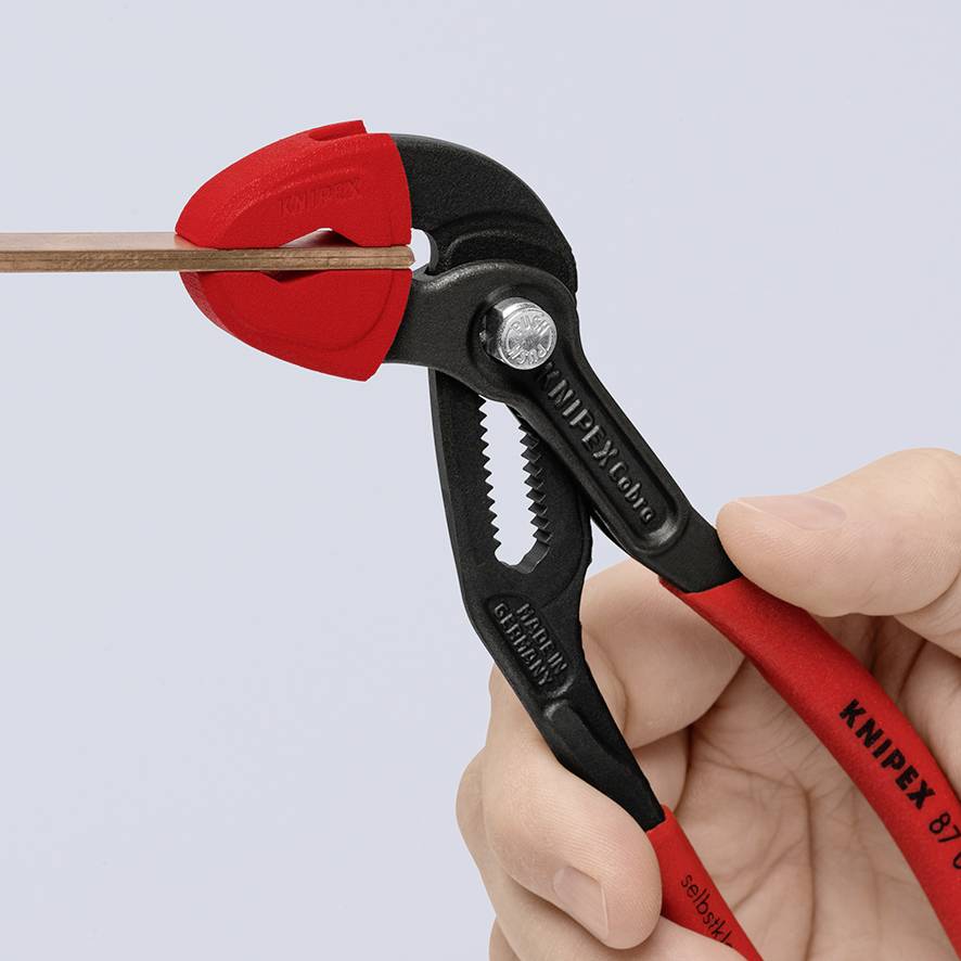 Červené kleště stříhají tenký hnědý kabel. Kleště jsou drženy rukou a vykazují detailní design.