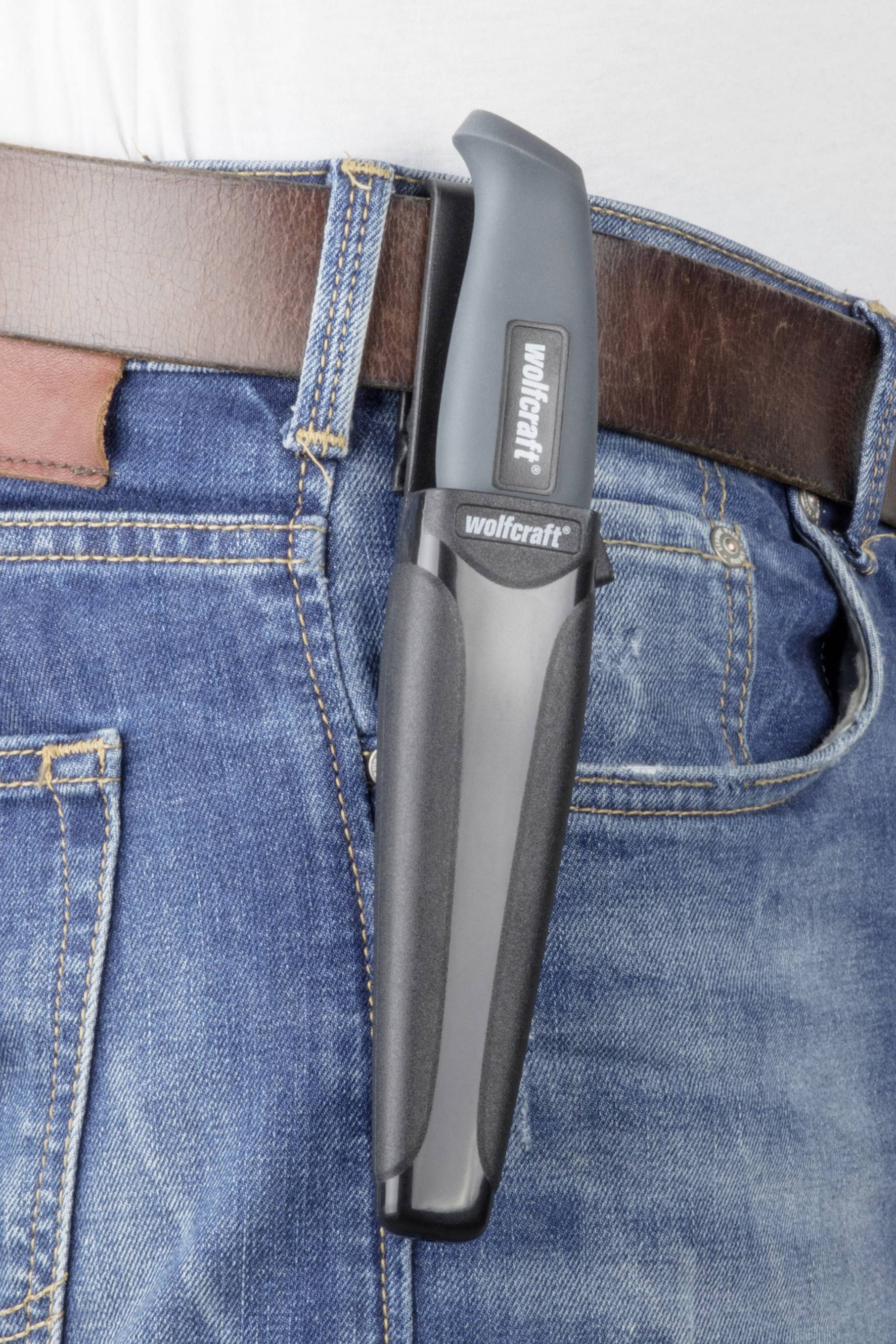 Nůž v robustním pouzdře připevněném k opasku džín. Označený logem 'wolfcraft', ukazuje praktický aspekt pro řemeslníky.